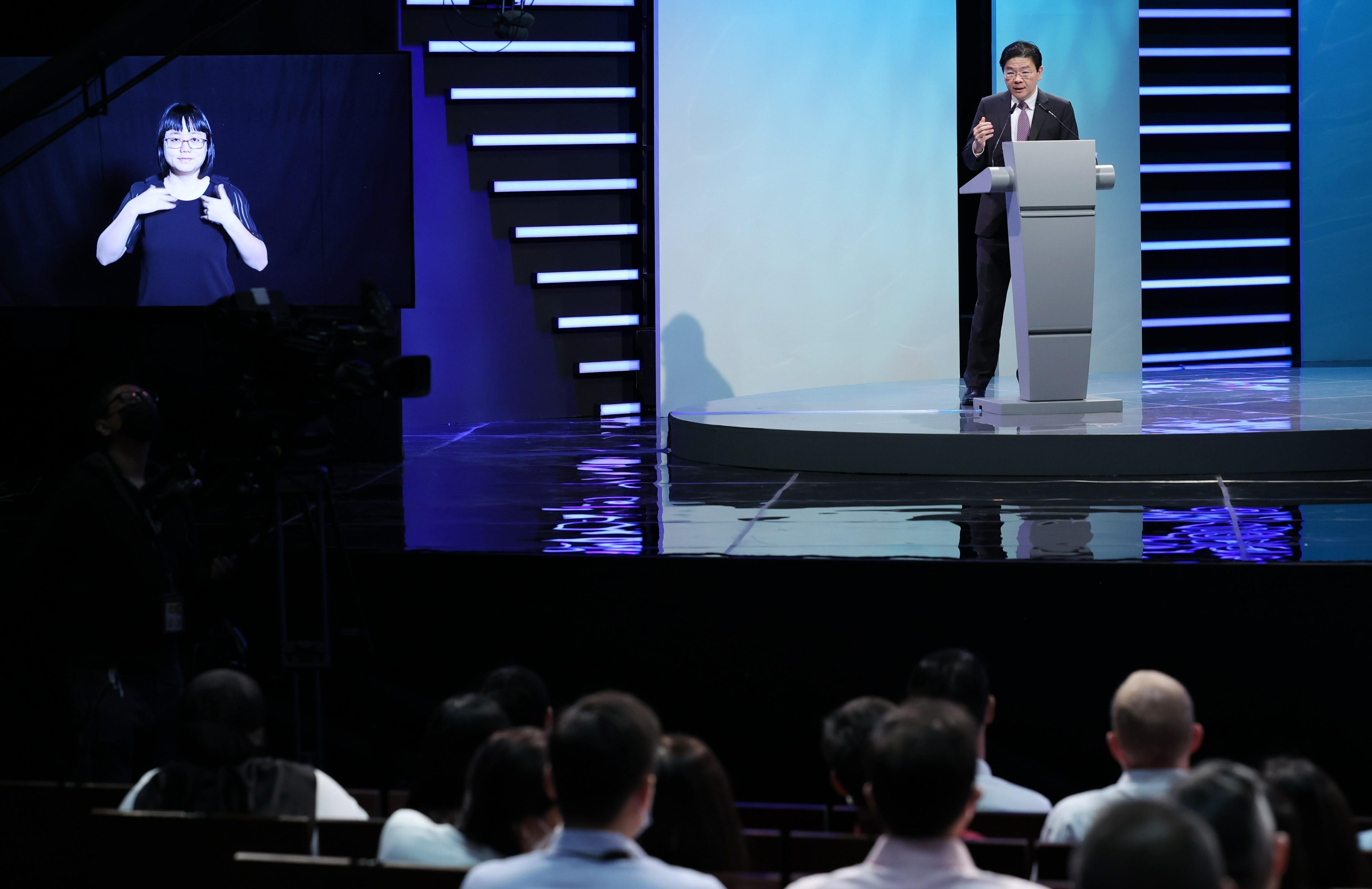 Speaker at podium with sign language interpreter, audience visible.