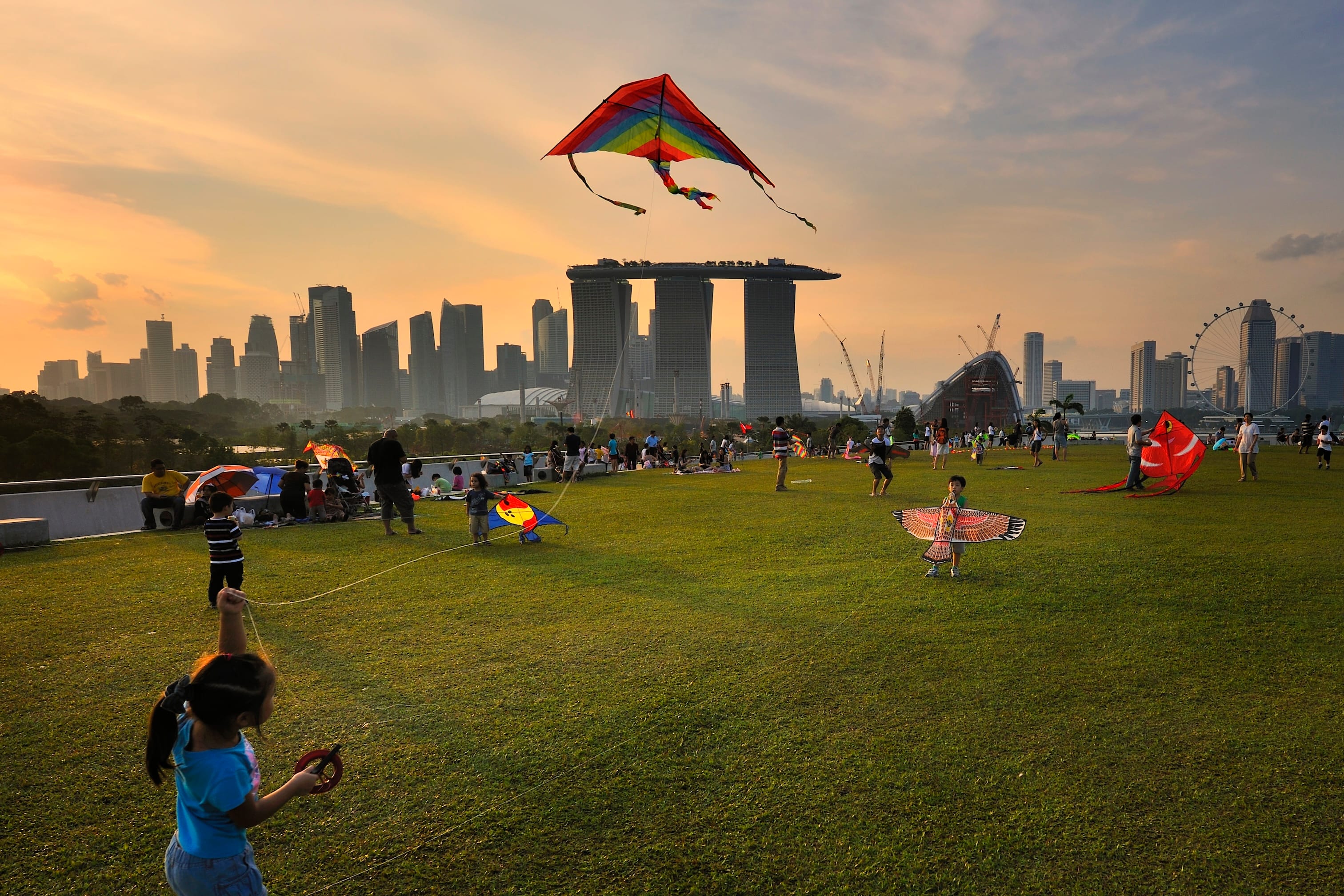 Families flying kites with Marina Bay Sands in the background during sunset.
