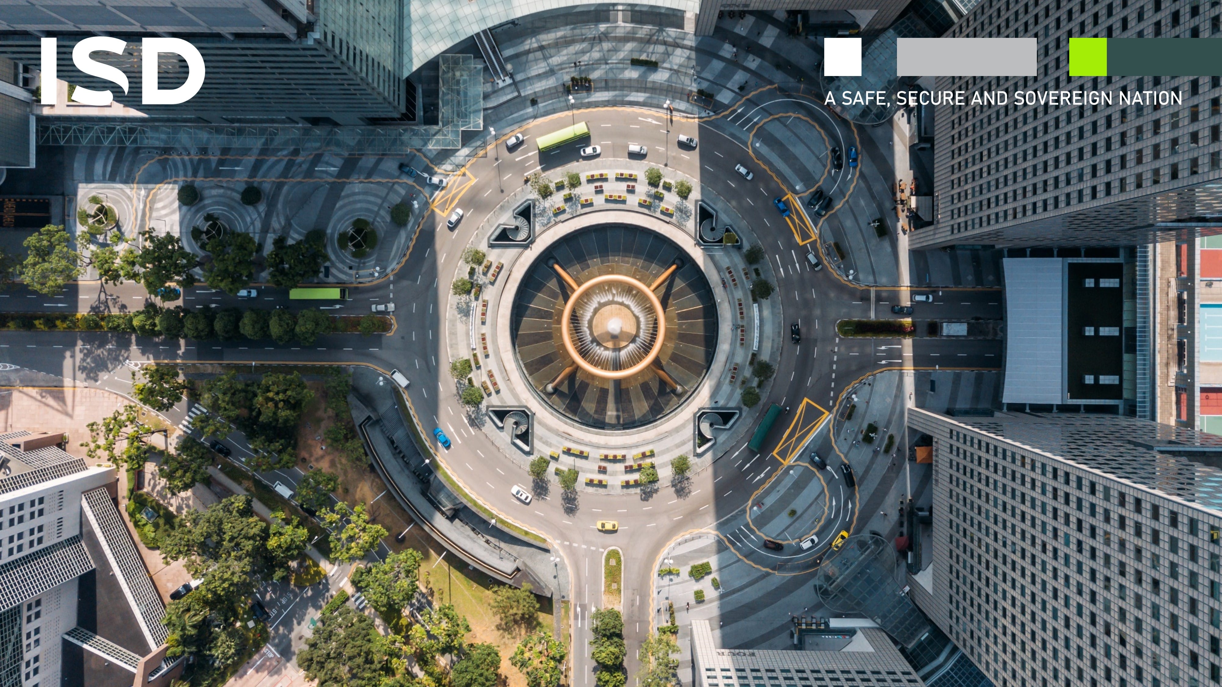Aerial view of a circular road with a fountain in the middle, surrounded by tall buildings.