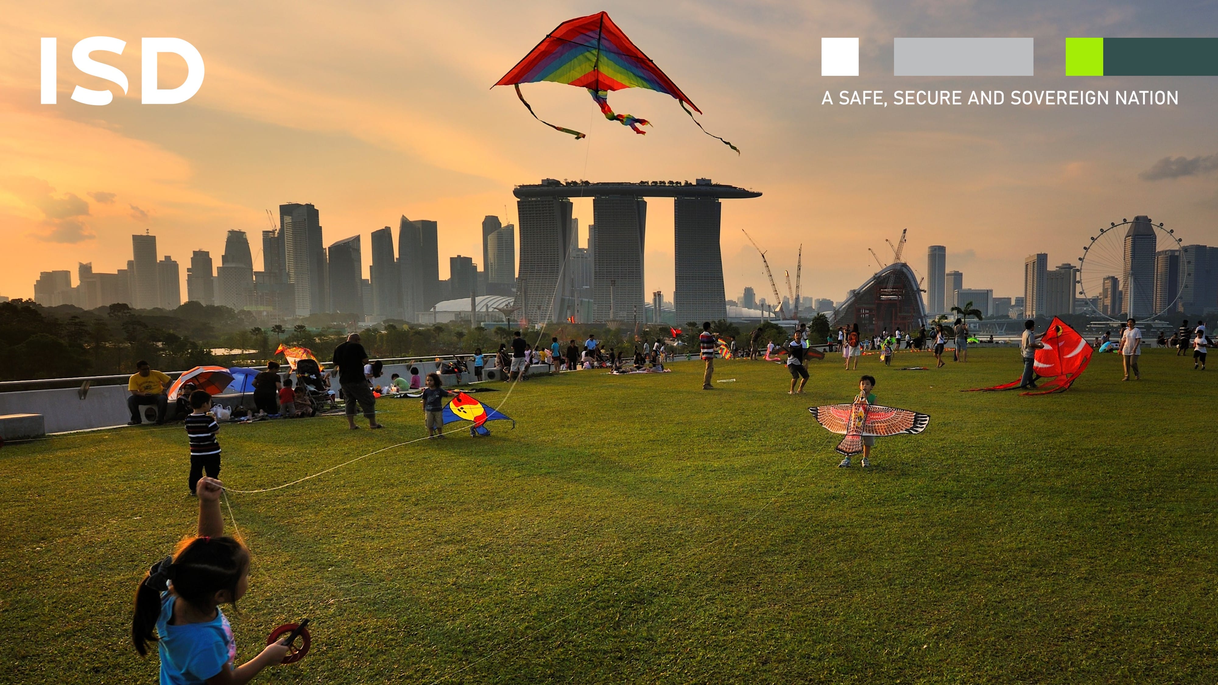 Families flying kites with Marina Bay Sands in the background during sunset.