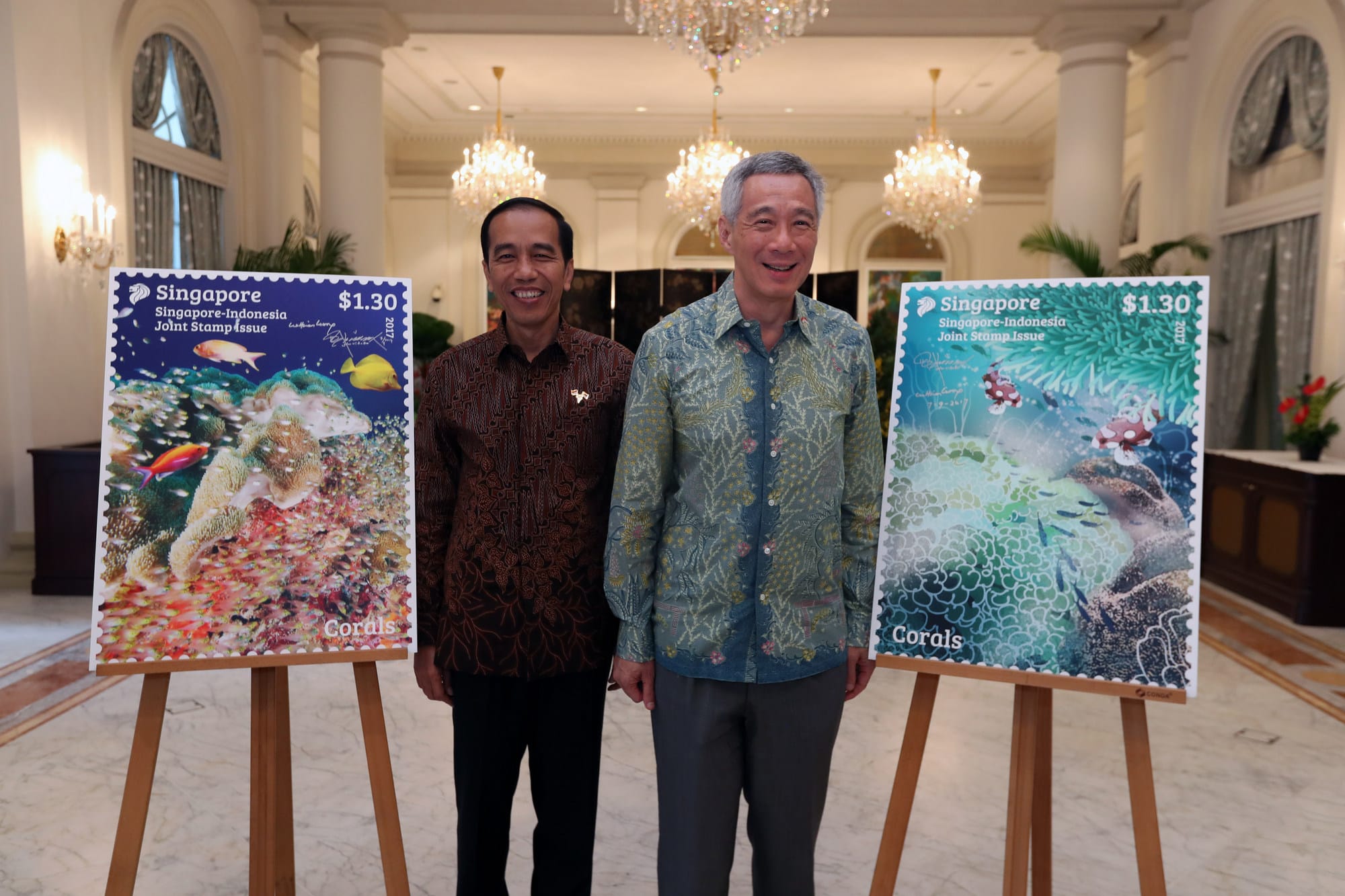 Two men stand behind easels displaying "Singapore-Indonesia Joint Stamp Issue" themed "Corals."