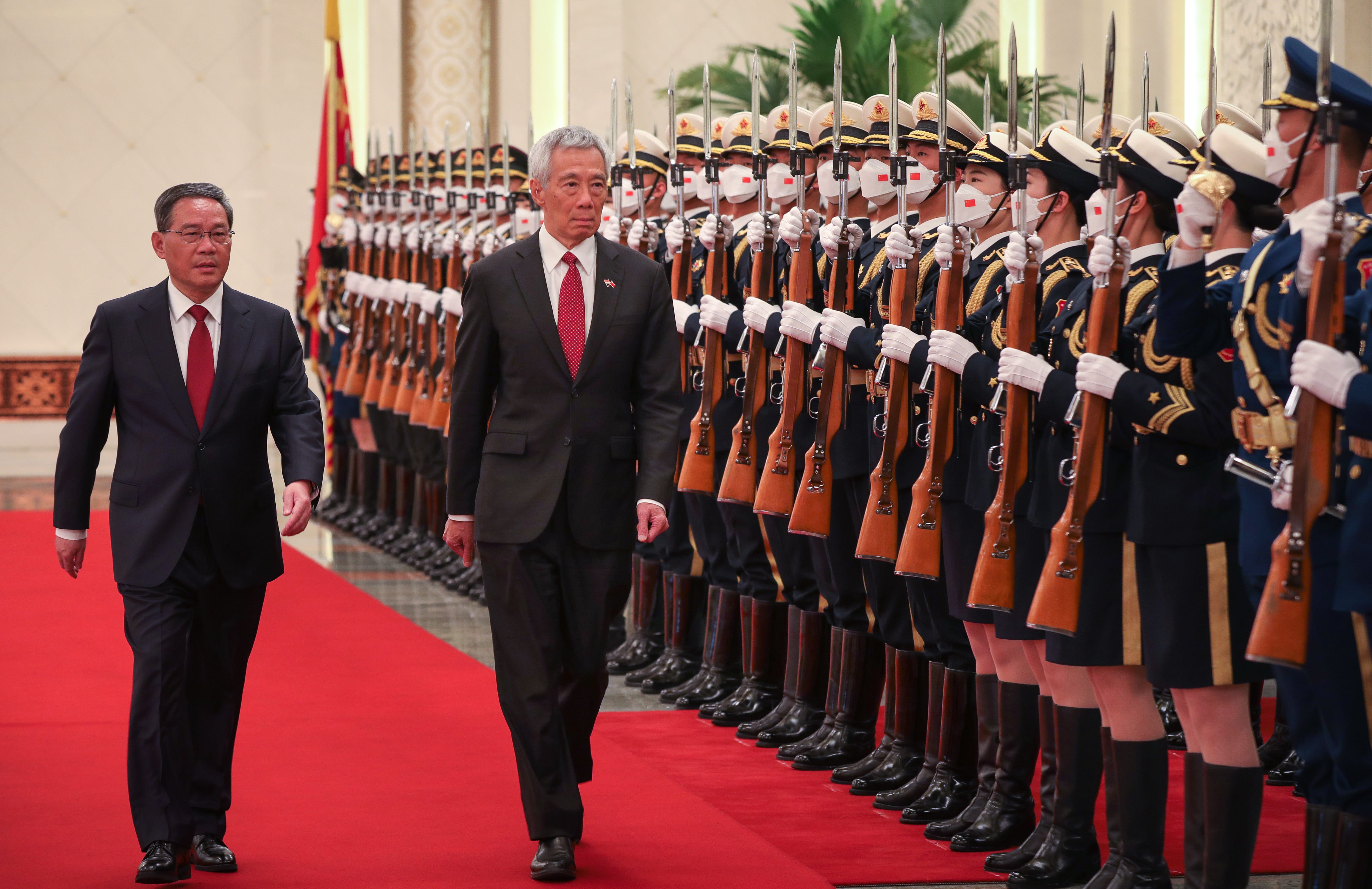 Two men in suits walk past a guard of honor with rifles and masks.