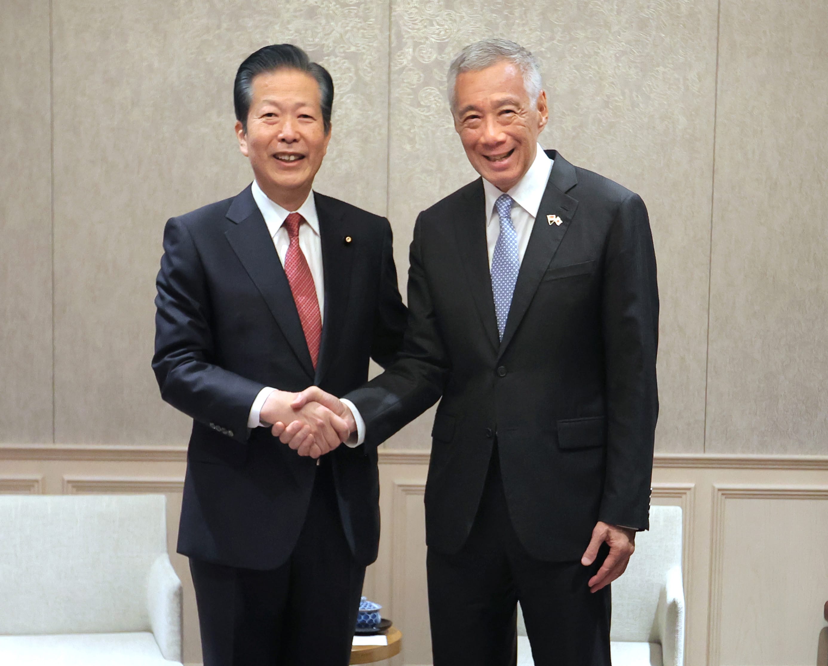 Two men in suits shaking hands, one wearing a Japan pin and the other, Singapore and Japan.