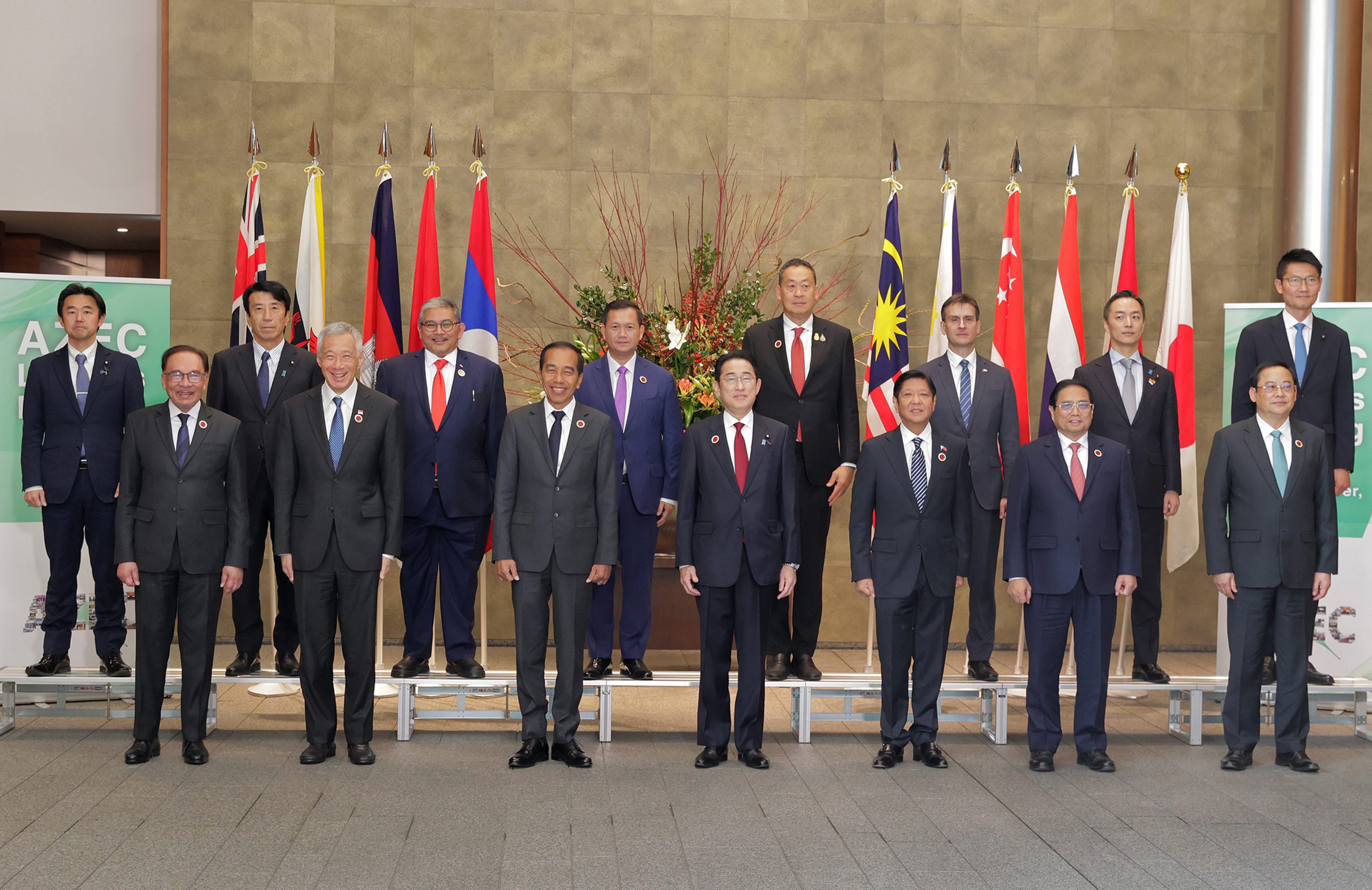 Group of dignitaries in suits posing before flags in a conference room.