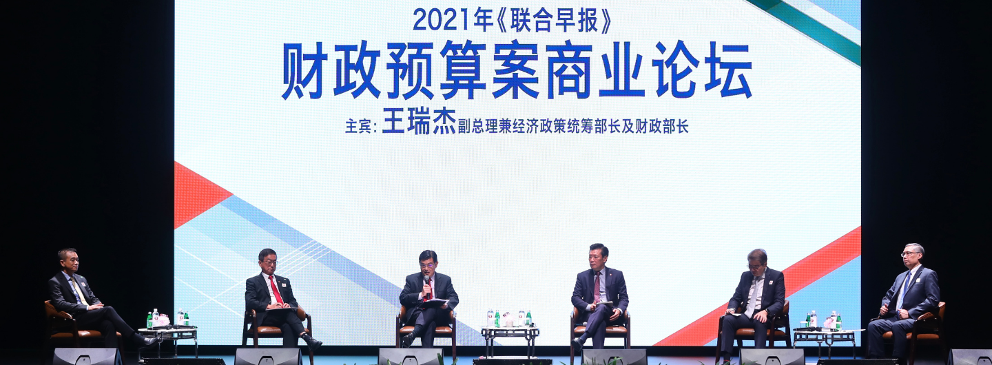 Five men in suits sit onstage before a screen with Chinese text.