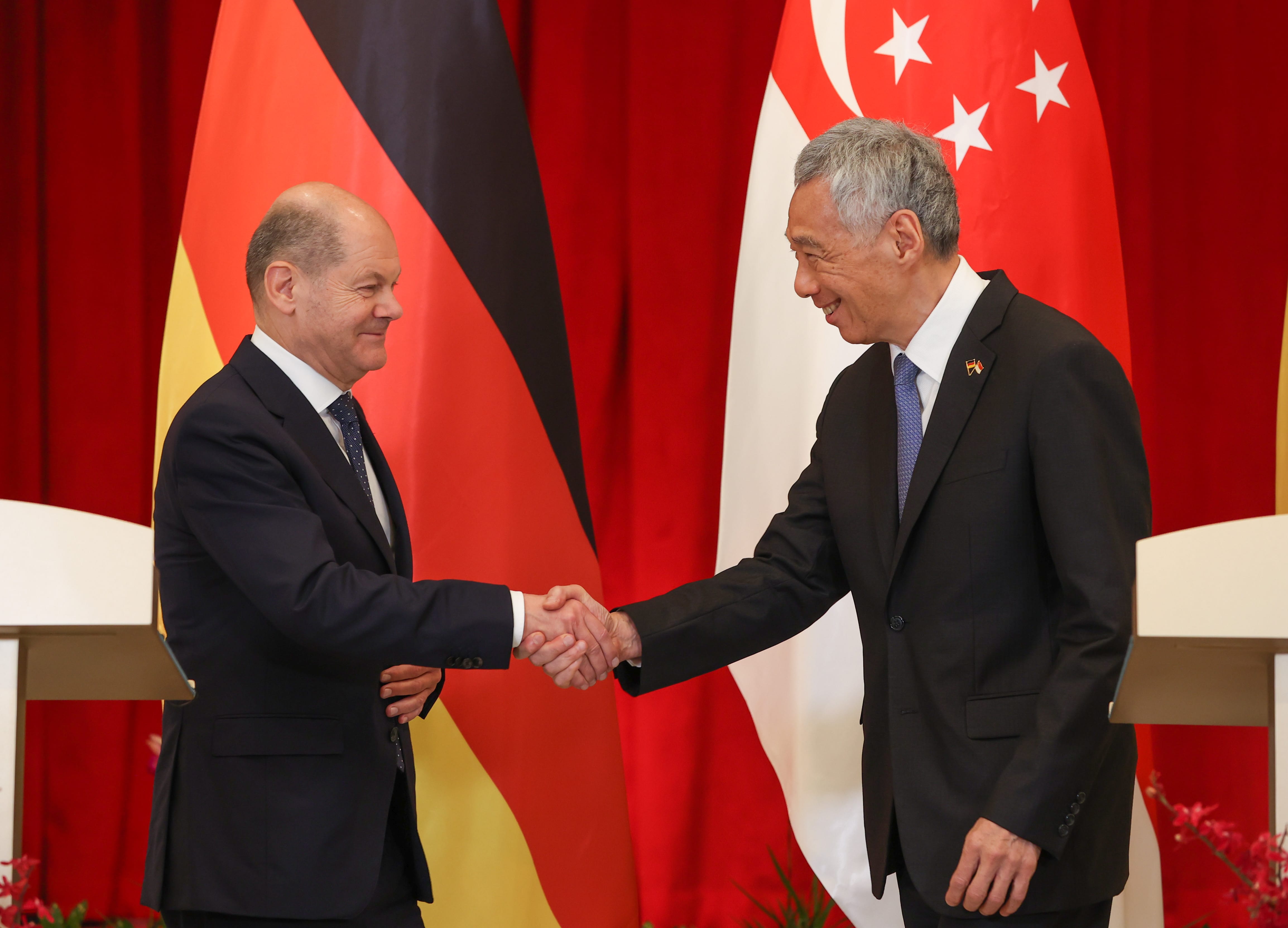 Olaf Scholz and Lee Hsien Loong shake hands before German and Singaporean flags.