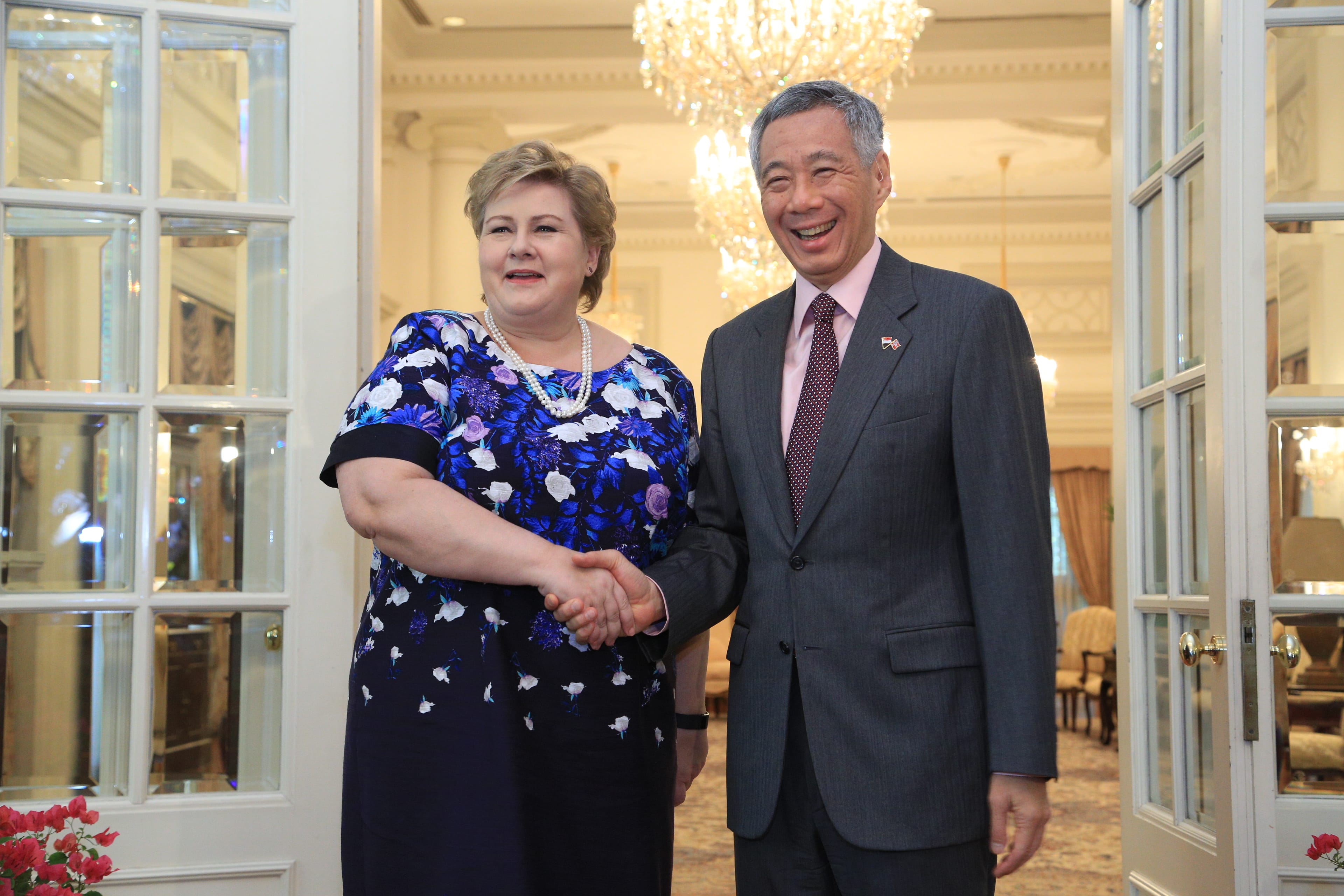 Erna Solberg & Lee Hsien Loong shaking hands in front of white doors and a chandelier.