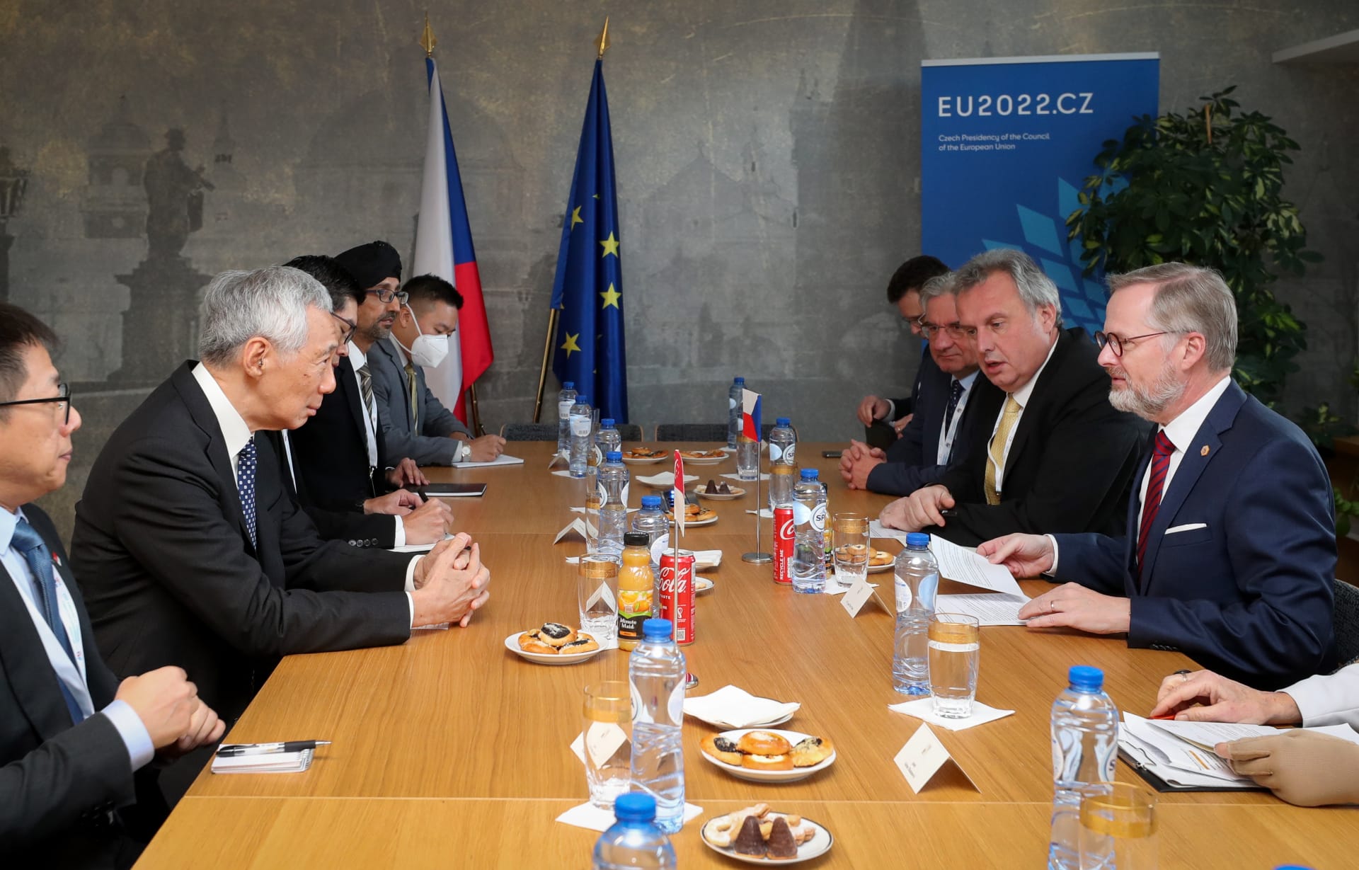 Meeting with officials seated at a long table, flags, food, and drinks present. "EU2022.CZ" banner visible.