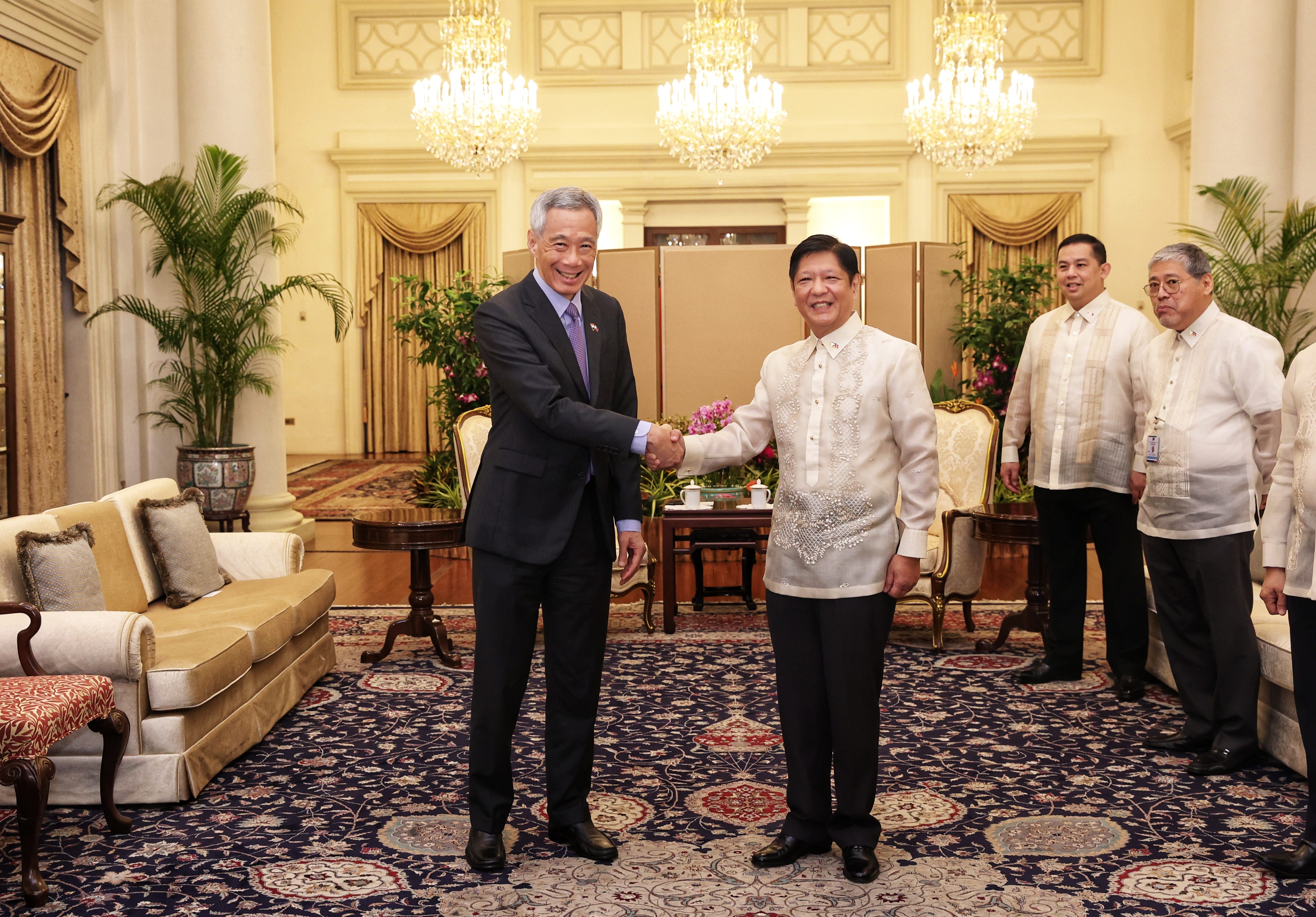 Lee Hsien Loong and Ferdinand Marcos Jr. shake hands indoors with others standing nearby.