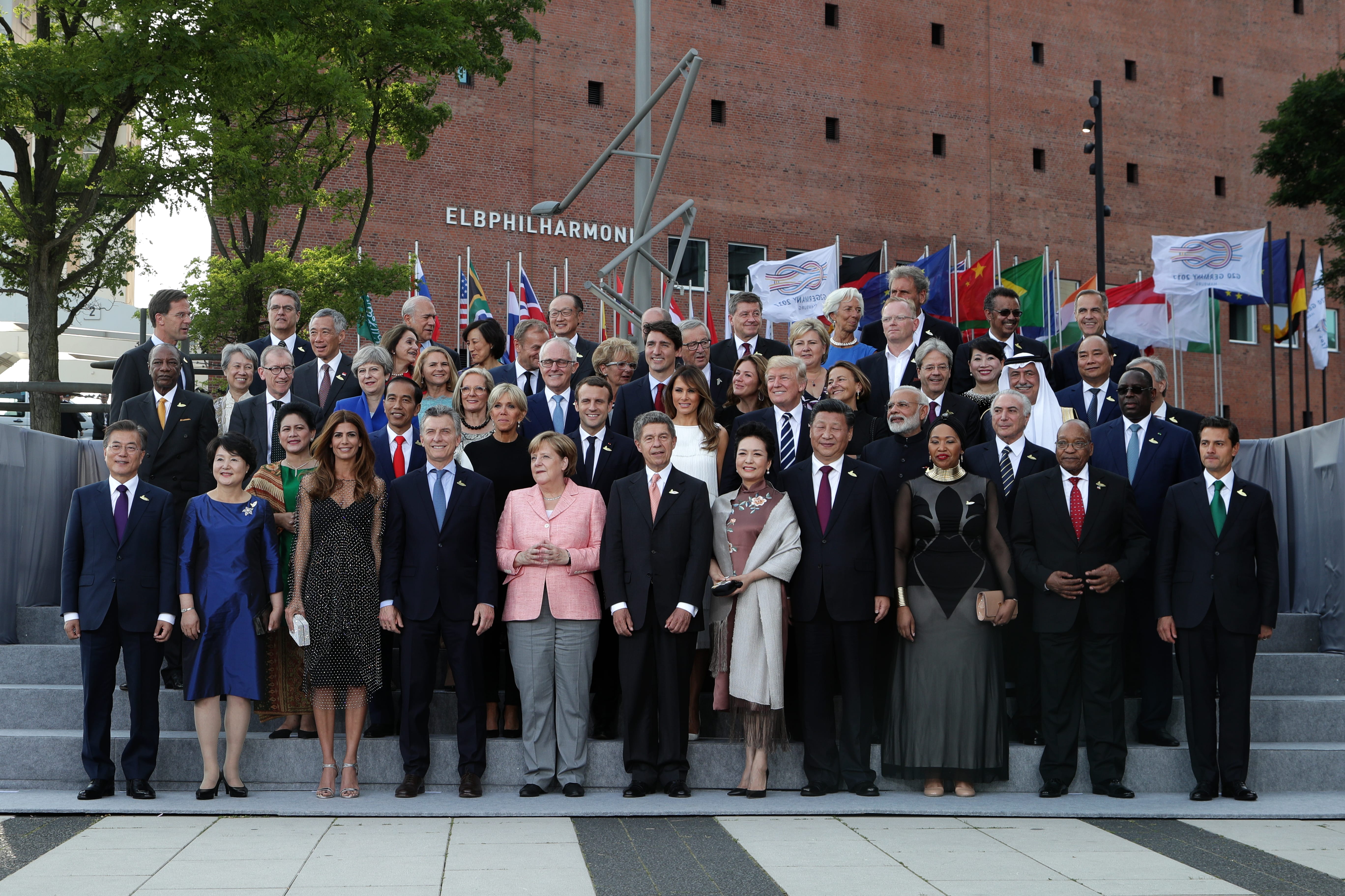 Group of world leaders on steps of Elbphilharmonie building with country flags.