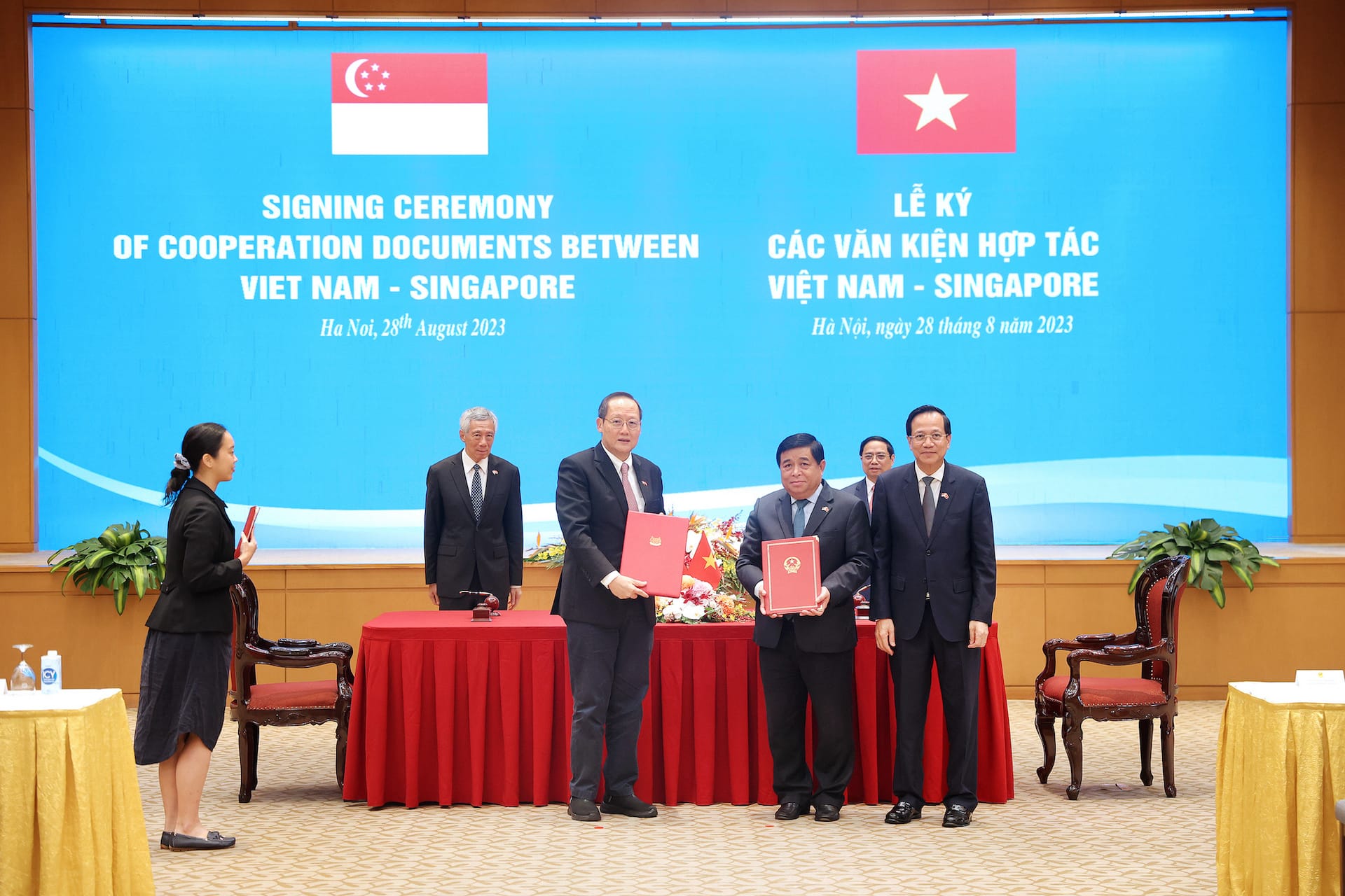 Signing ceremony with flags of Singapore and Vietnam. Officials holding documents.