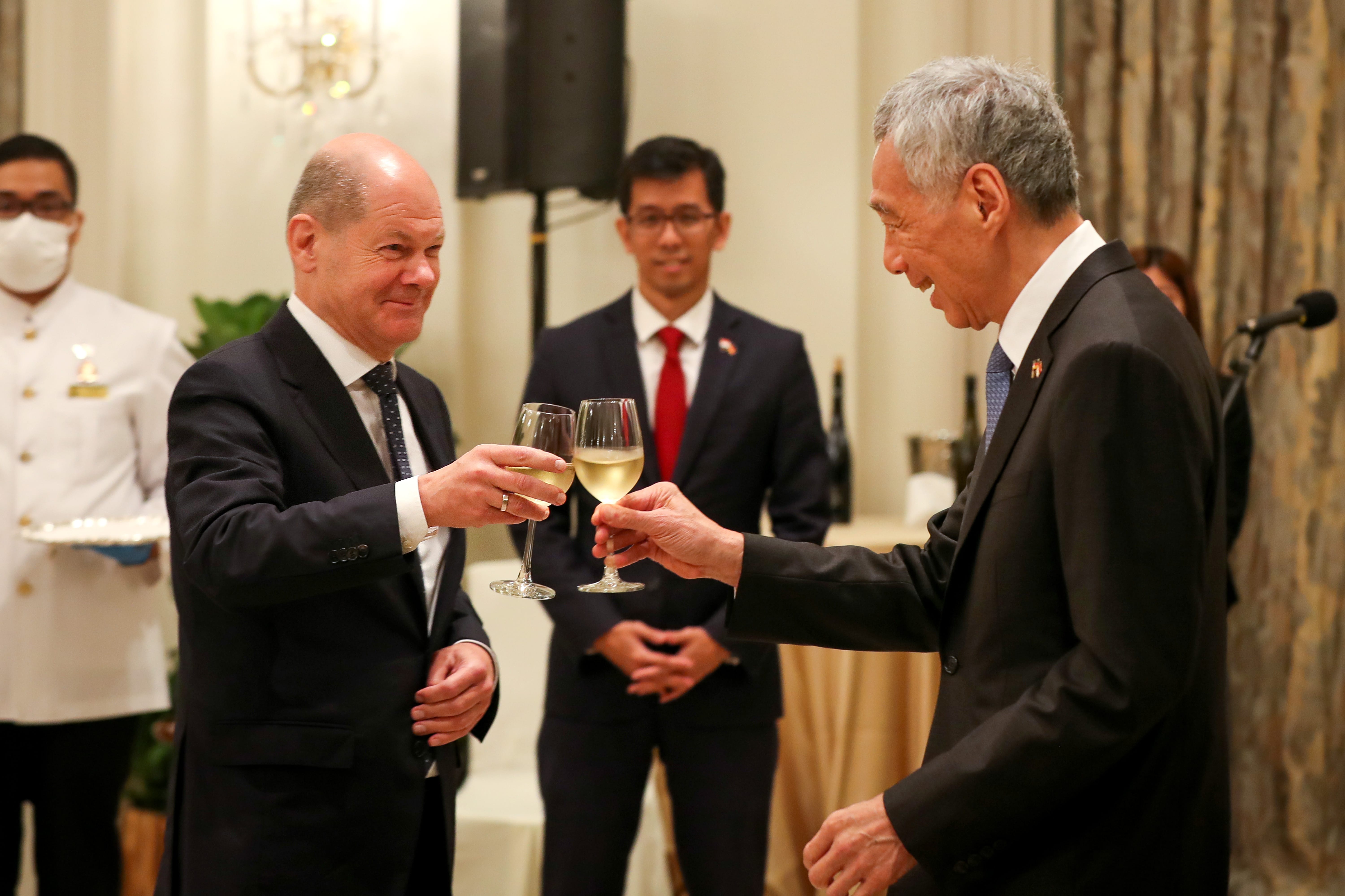 Olaf Scholz and Lee Hsien Loong toasting wine glasses, wearing suits indoors.
