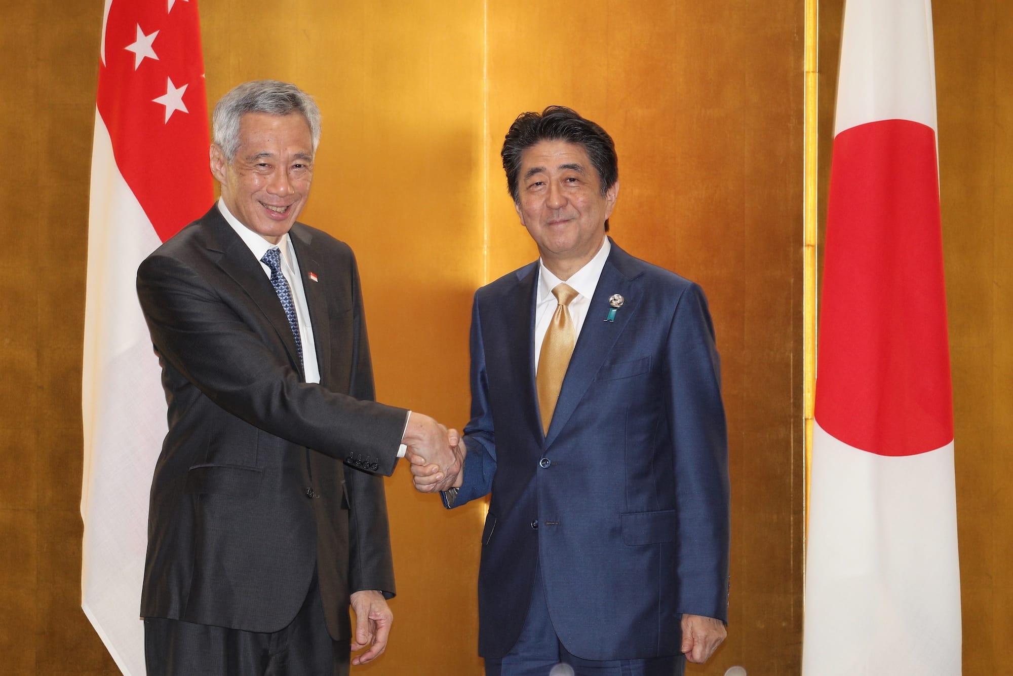 Lee Hsien Loong and Shinzo Abe shaking hands with Singapore and Japan flags behind.