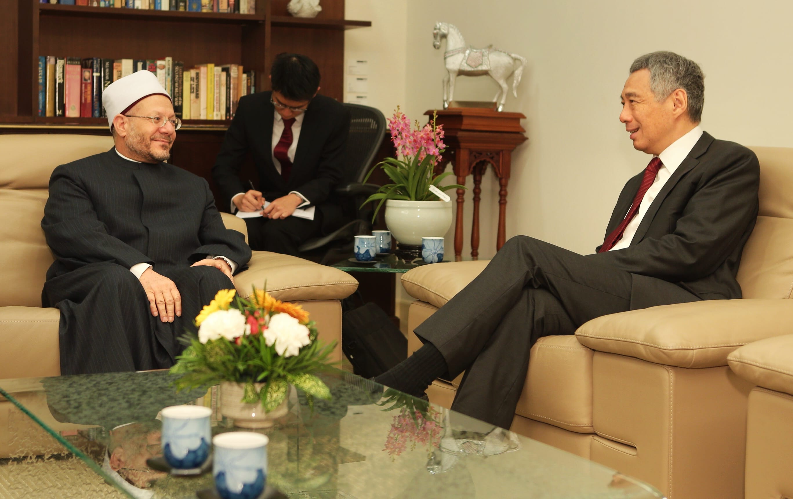 Lee Hsien Loong in a suit, seated and talking with a man in traditional Muslim attire.