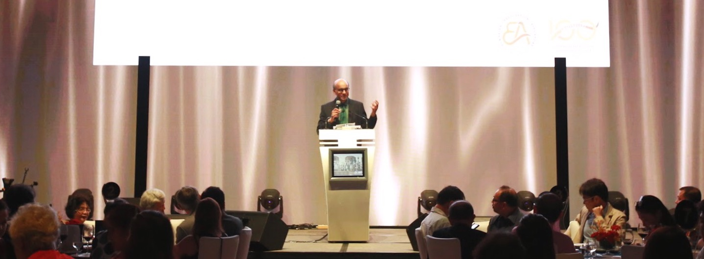 Speaker on stage giving a speech to seated attendees at an event.