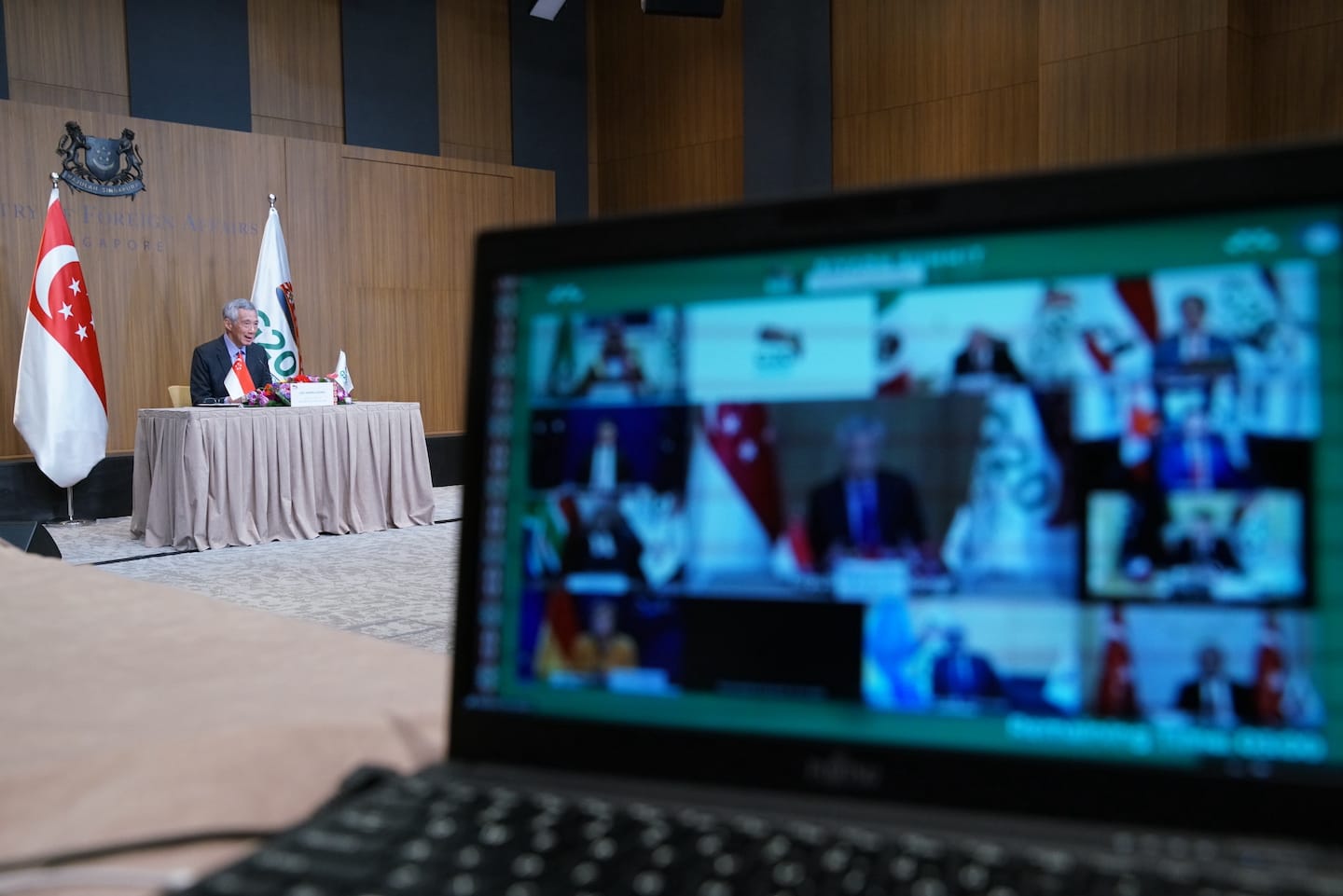 Laptop shows a video conference; Lee Hsien Loong sits at a desk with Singapore flag.