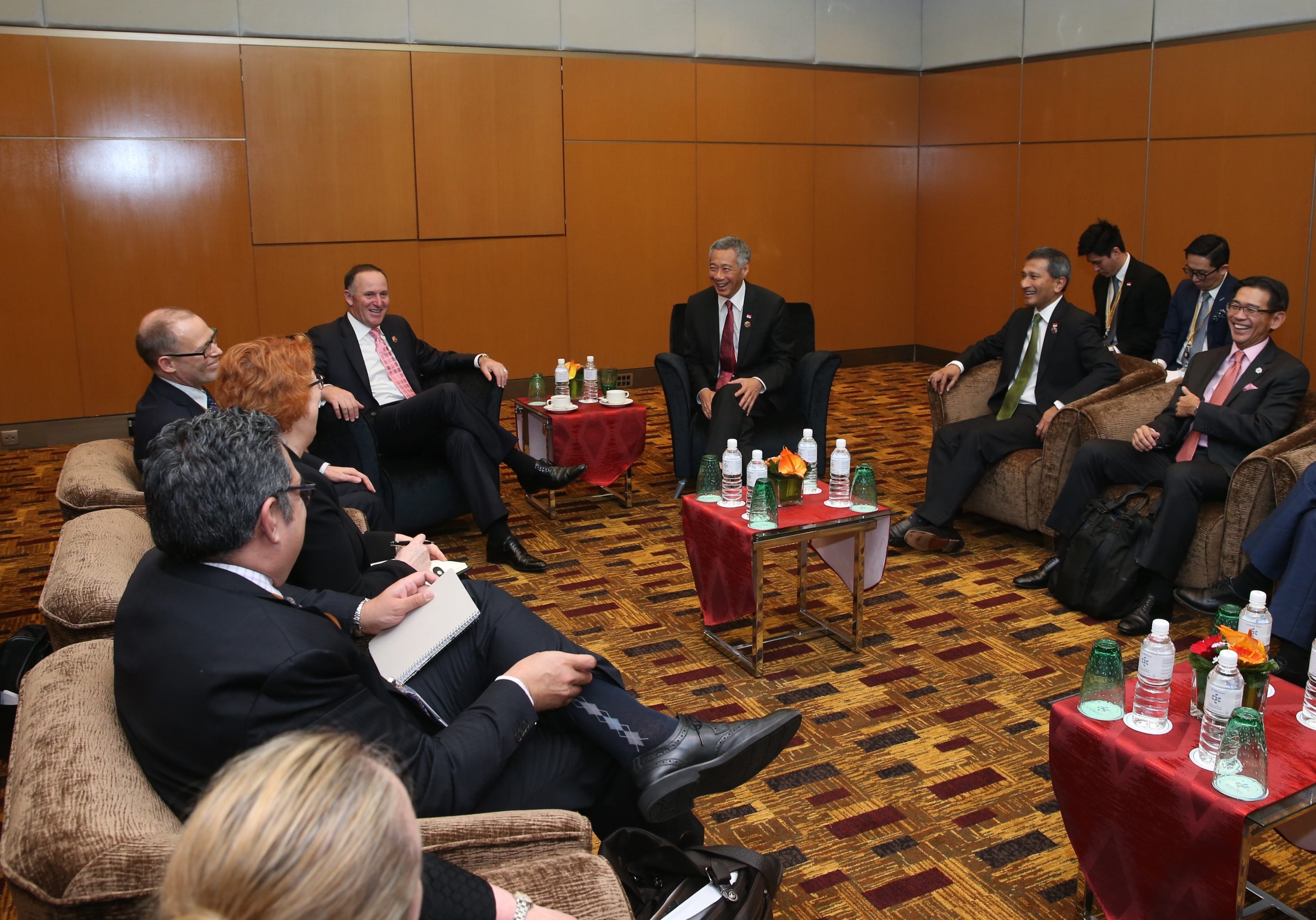 Group of people in suits seated around tables with drinks, indoors.