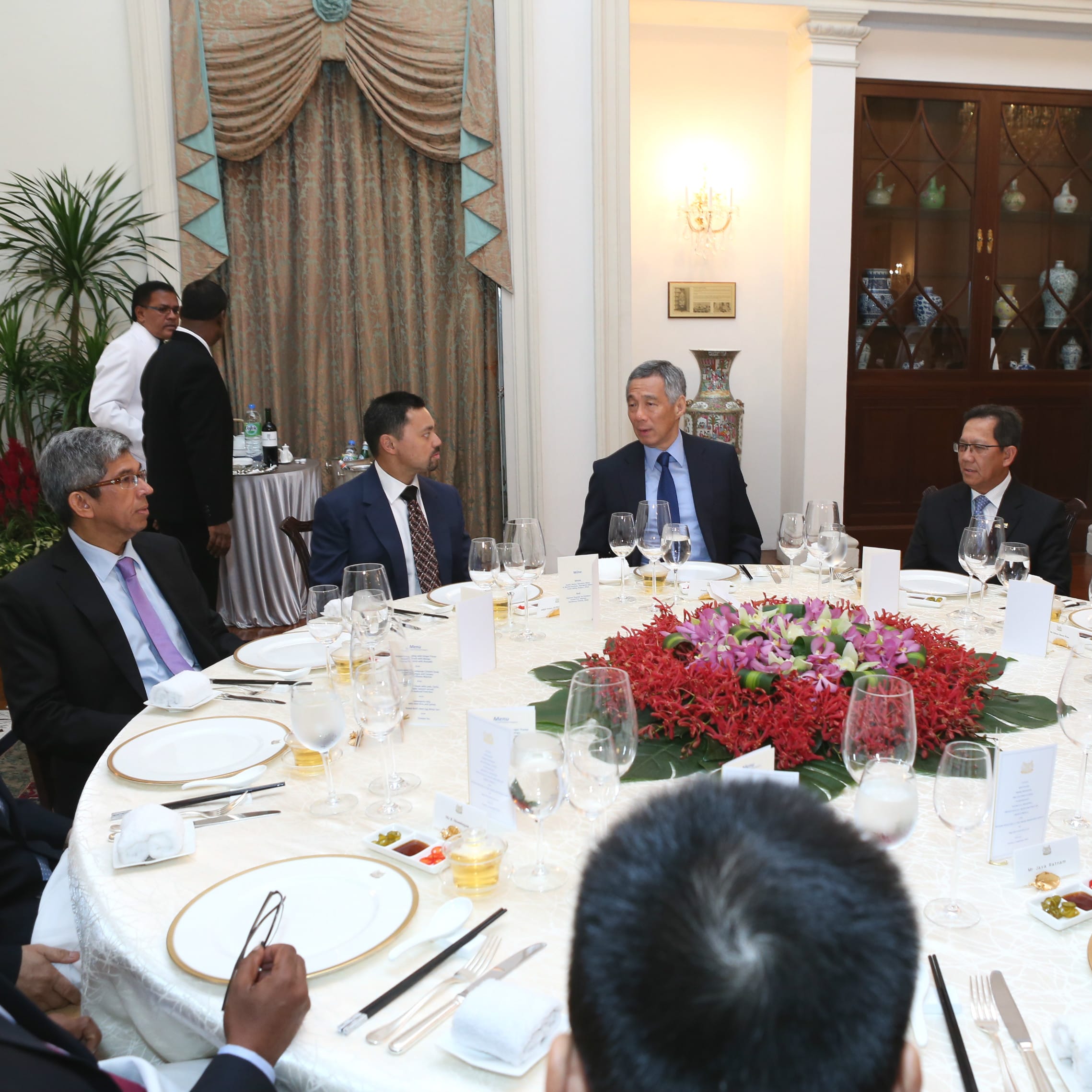 Lee Hsien Loong at round table with suited men, set with dishes and glasses.