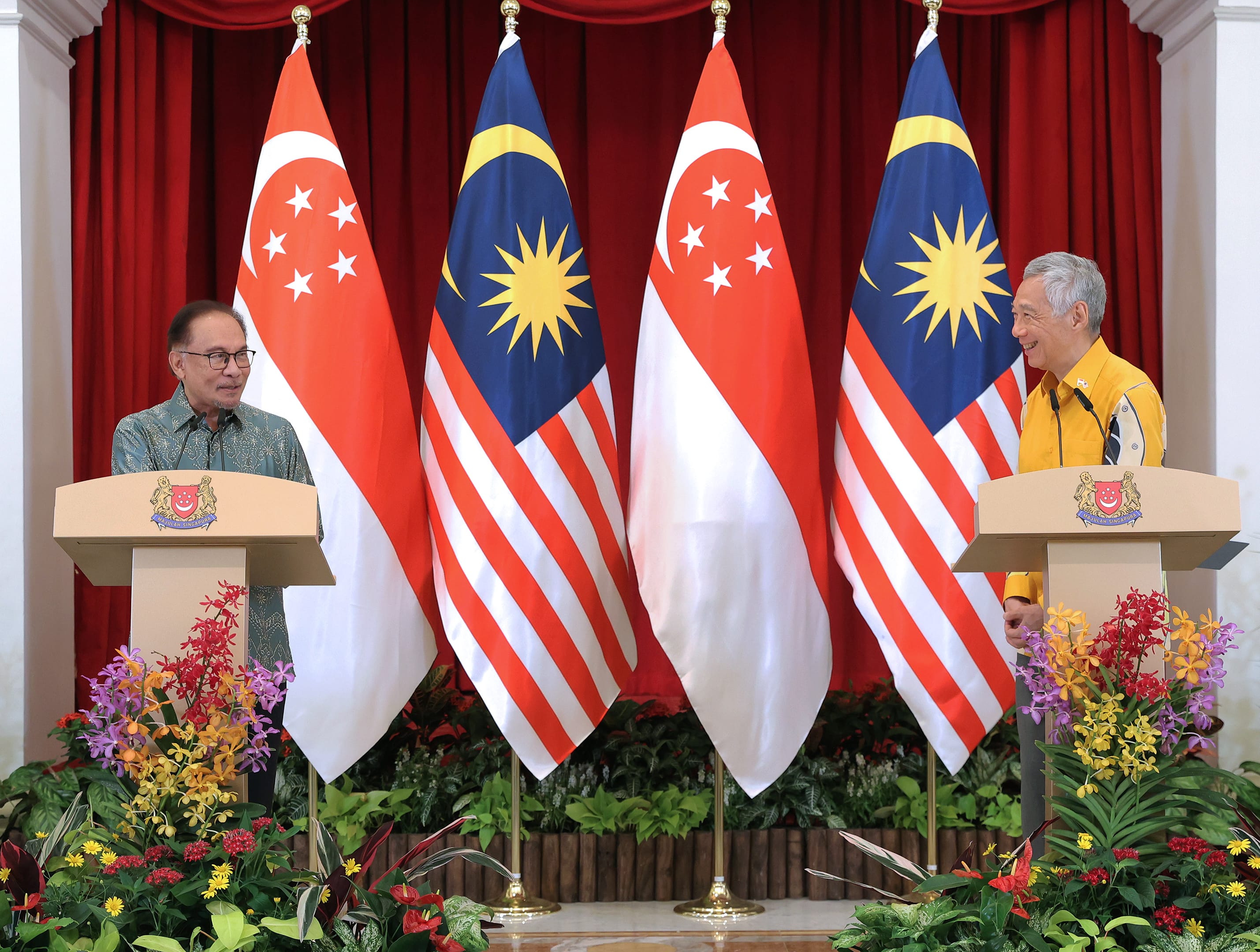 Anwar Ibrahim and Lee Hsien Loong at lecterns flanked by Singapore and Malaysia flags.