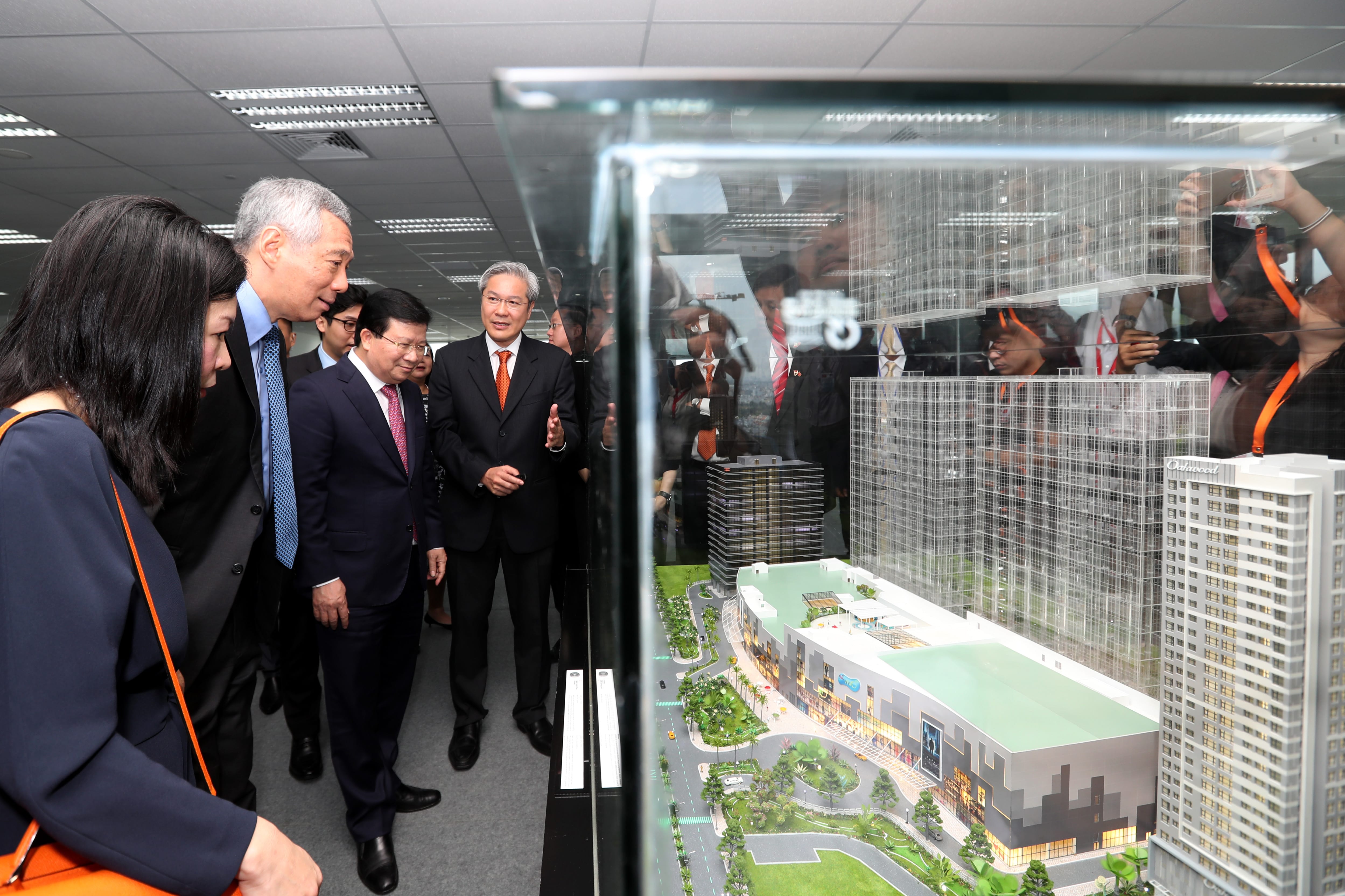 Group viewing architectural model of a building complex inside glass enclosure.