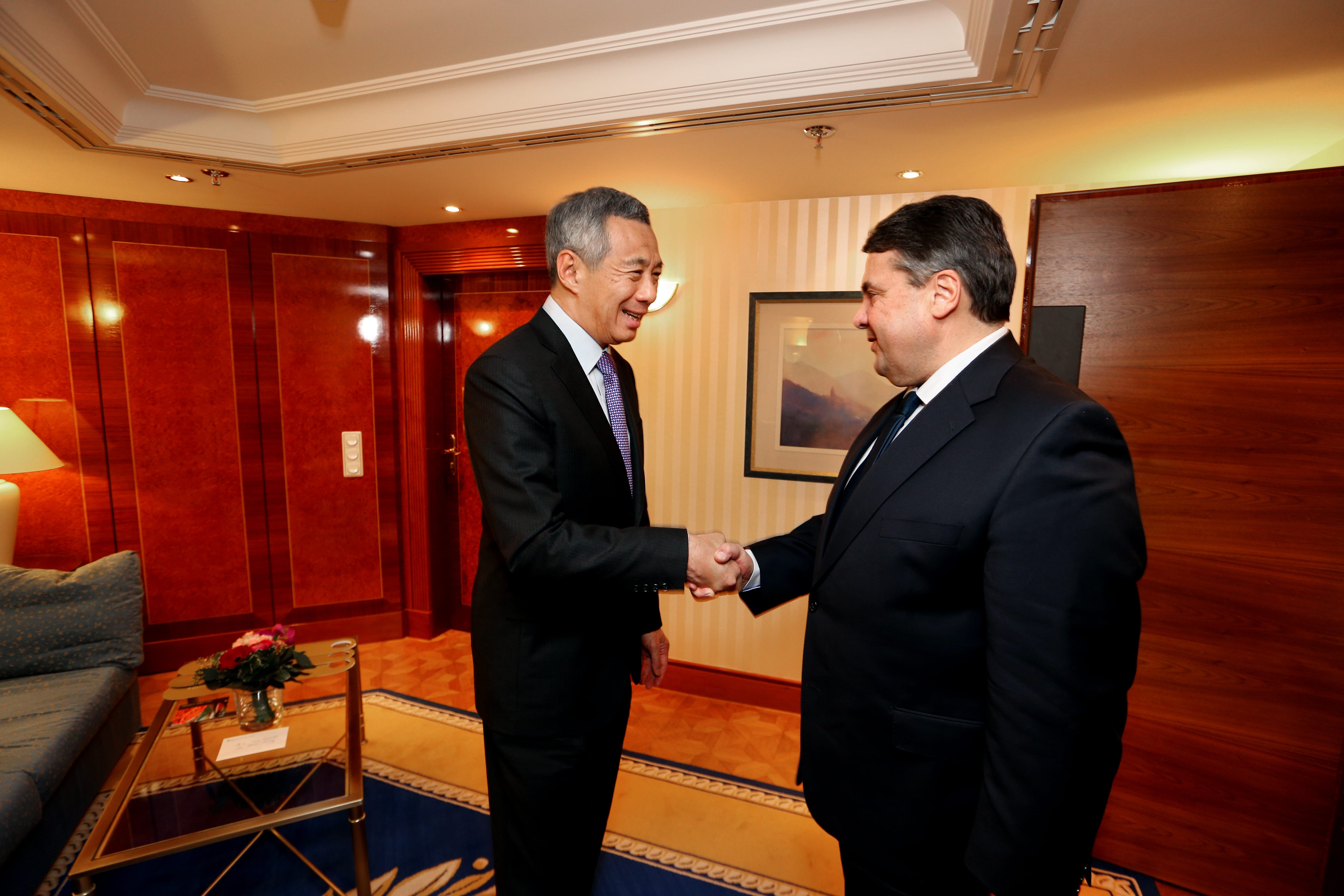 Two men in suits shaking hands in a wood-paneled room.