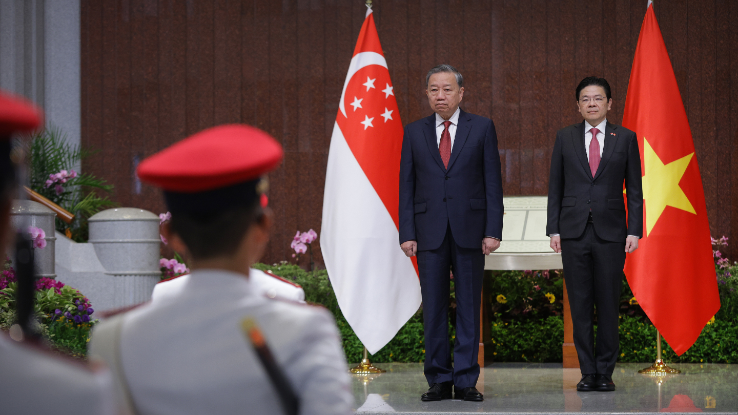 Two men in suits stand beside the Singapore and Vietnam flags, facing honor guard.