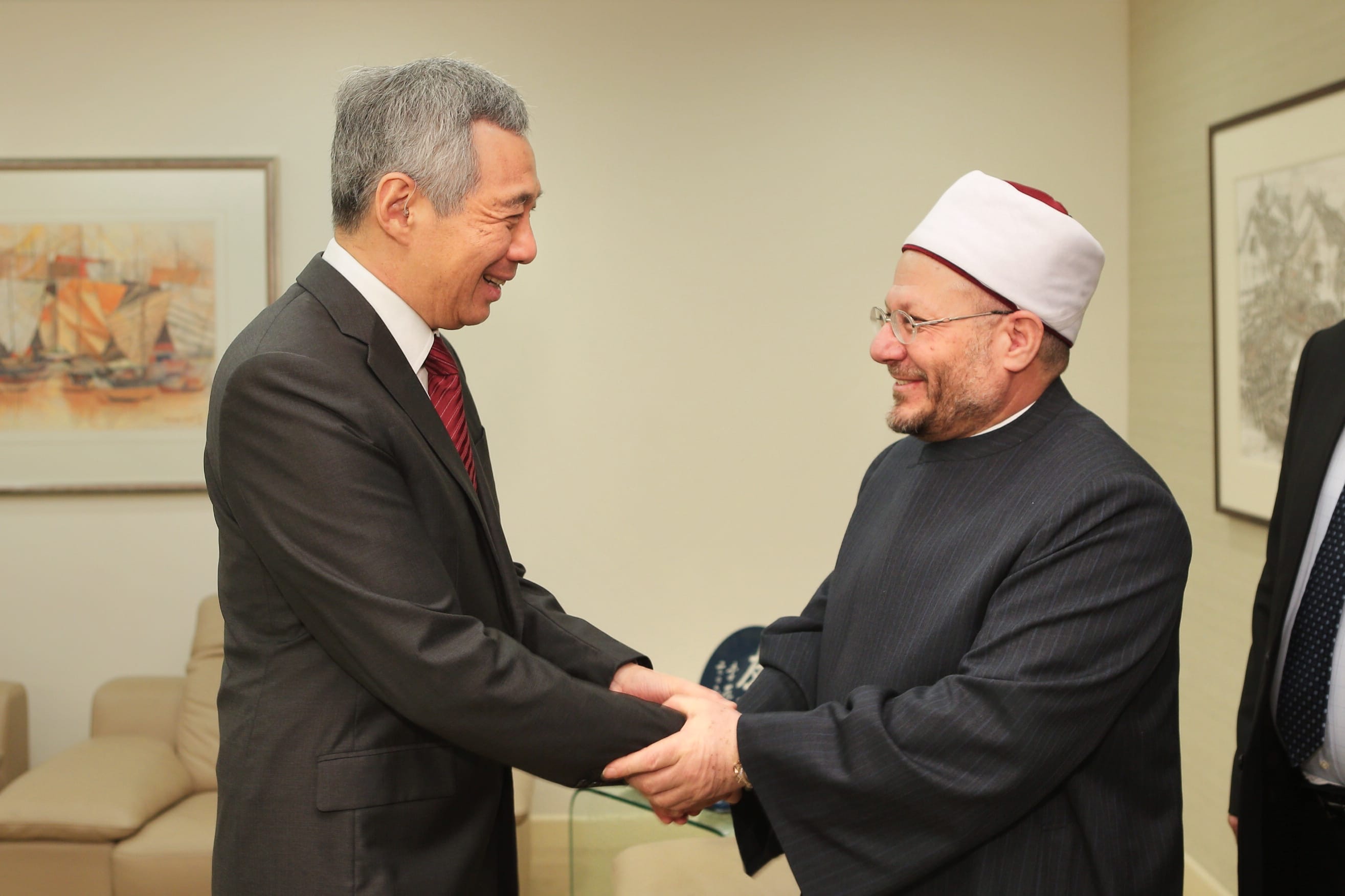 Lee Hsien Loong and a cleric shake hands in a room with a painting.
