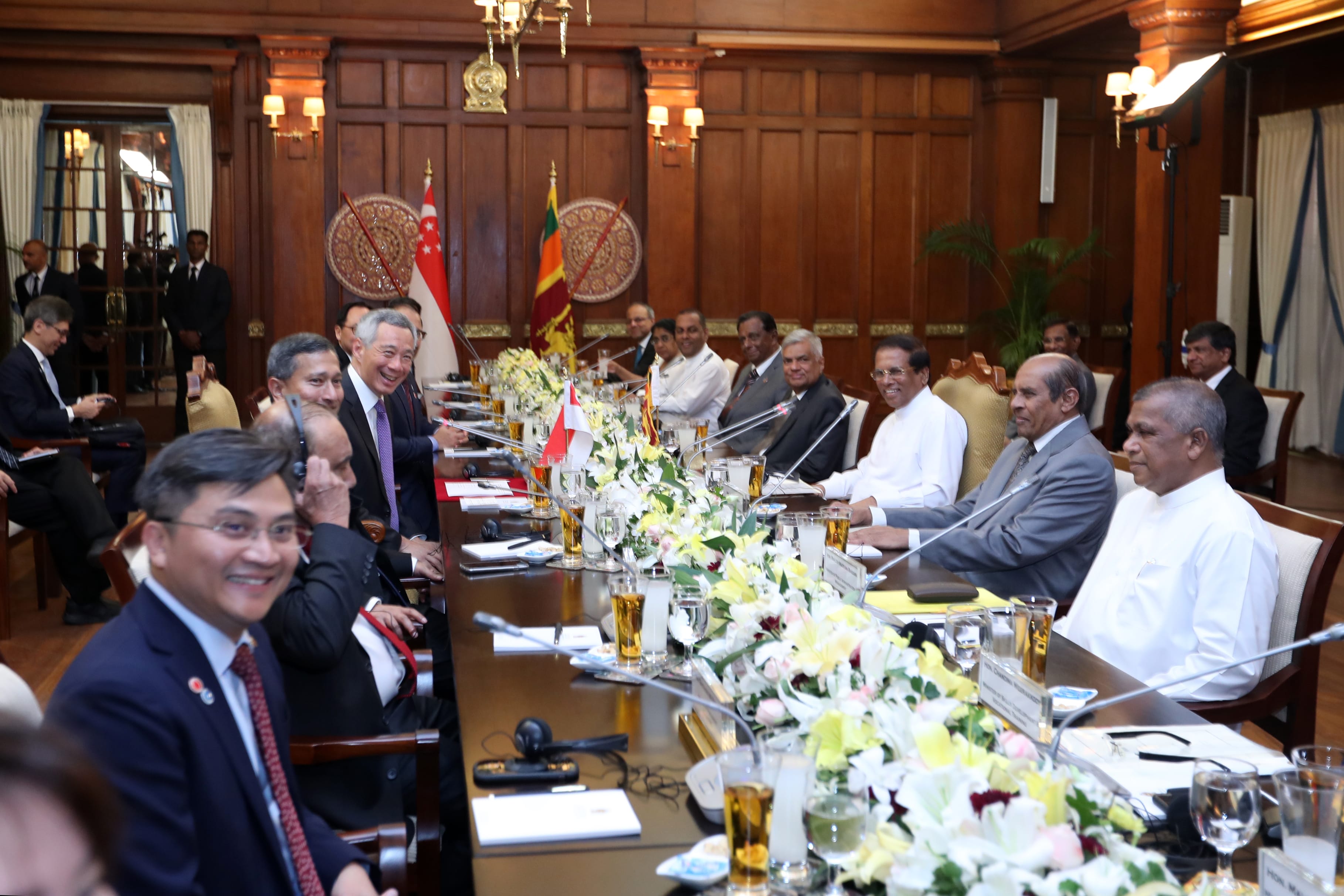 Meeting of delegates at a long table with Singapore and Sri Lanka flags in the background.