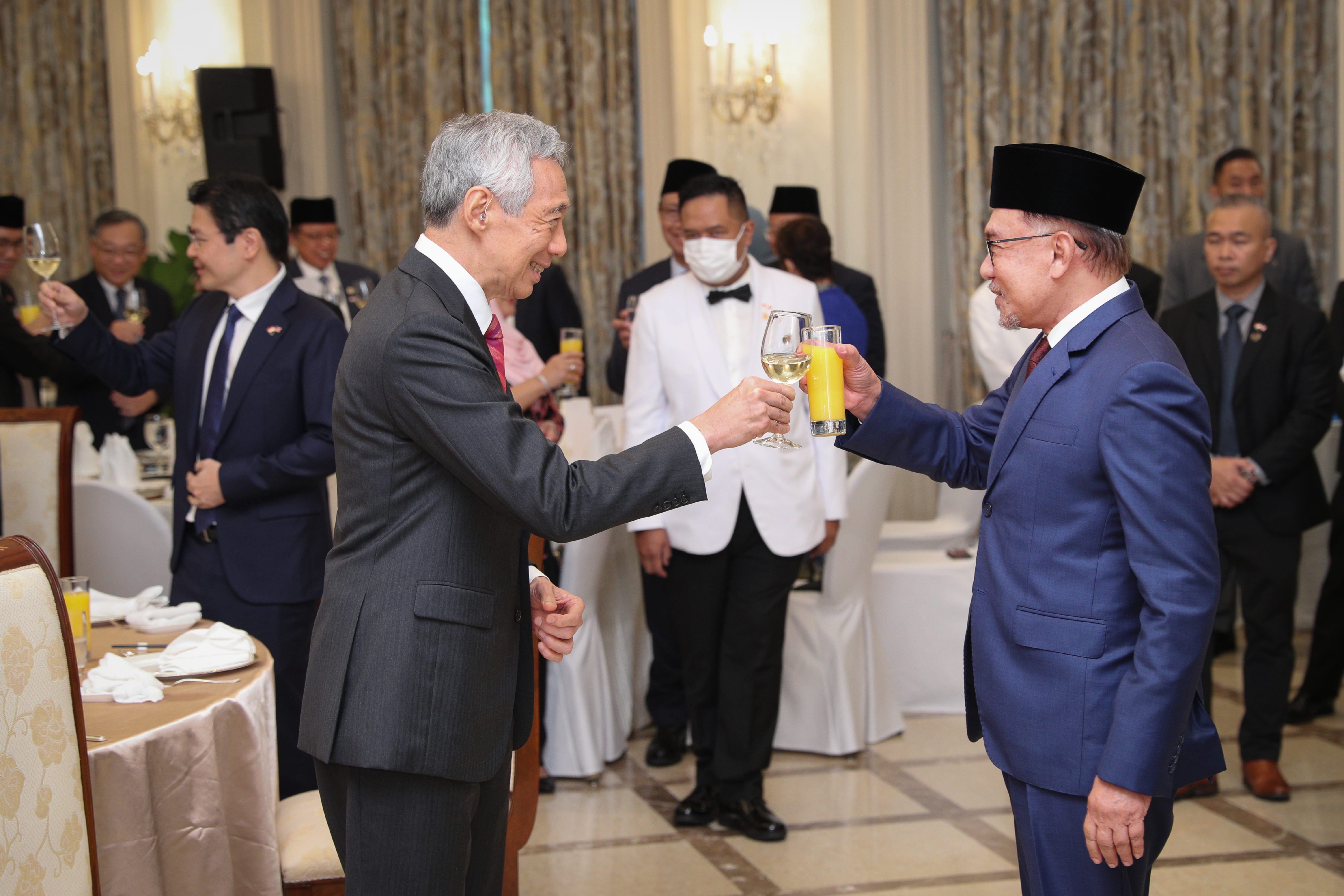 Lee Hsien Loong and Anwar Ibrahim toasting with wine and juice at an indoor event.