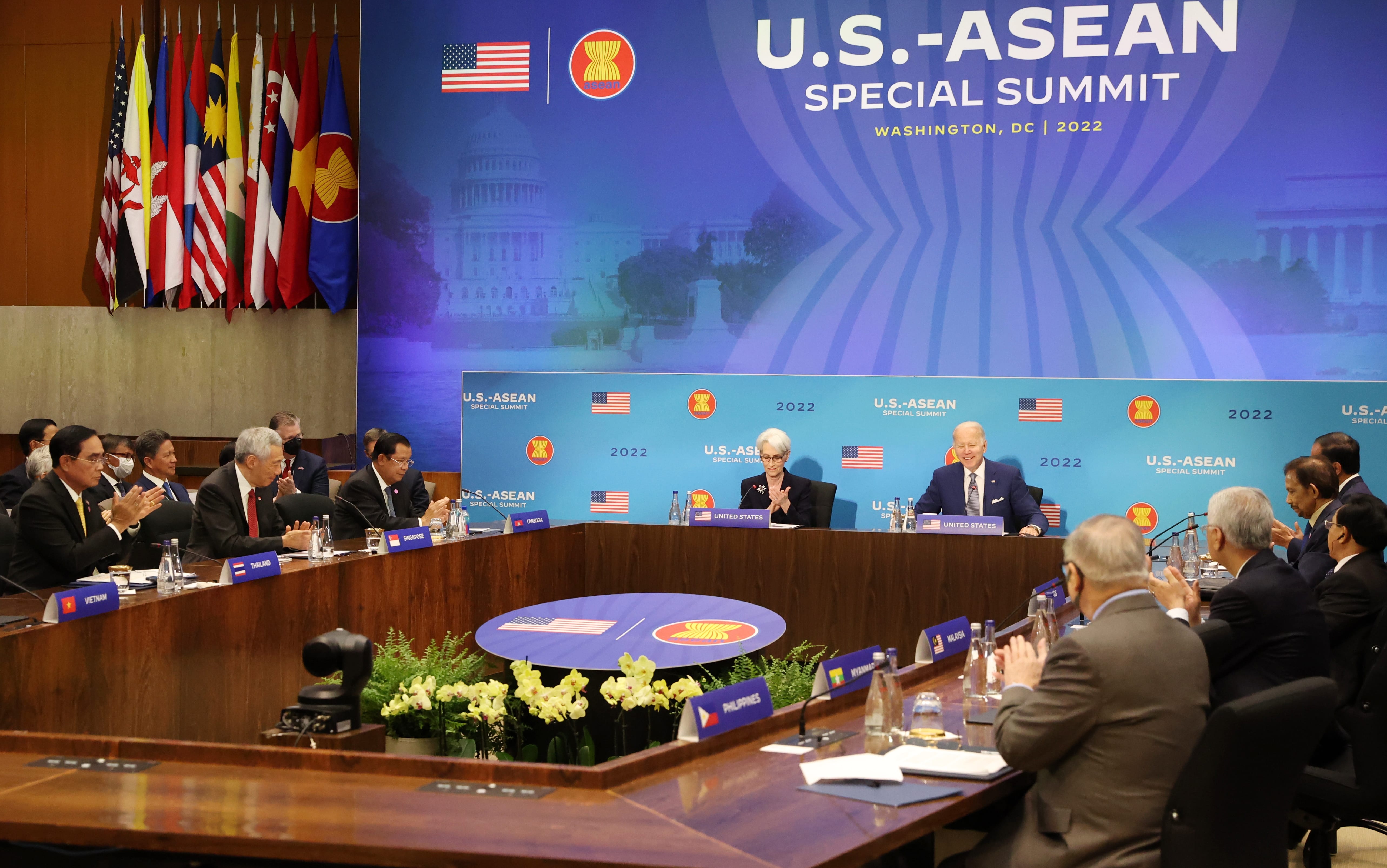 US-ASEAN Summit with flags, placards, and attendees at a large table. Biden and Harris seated at the head table.