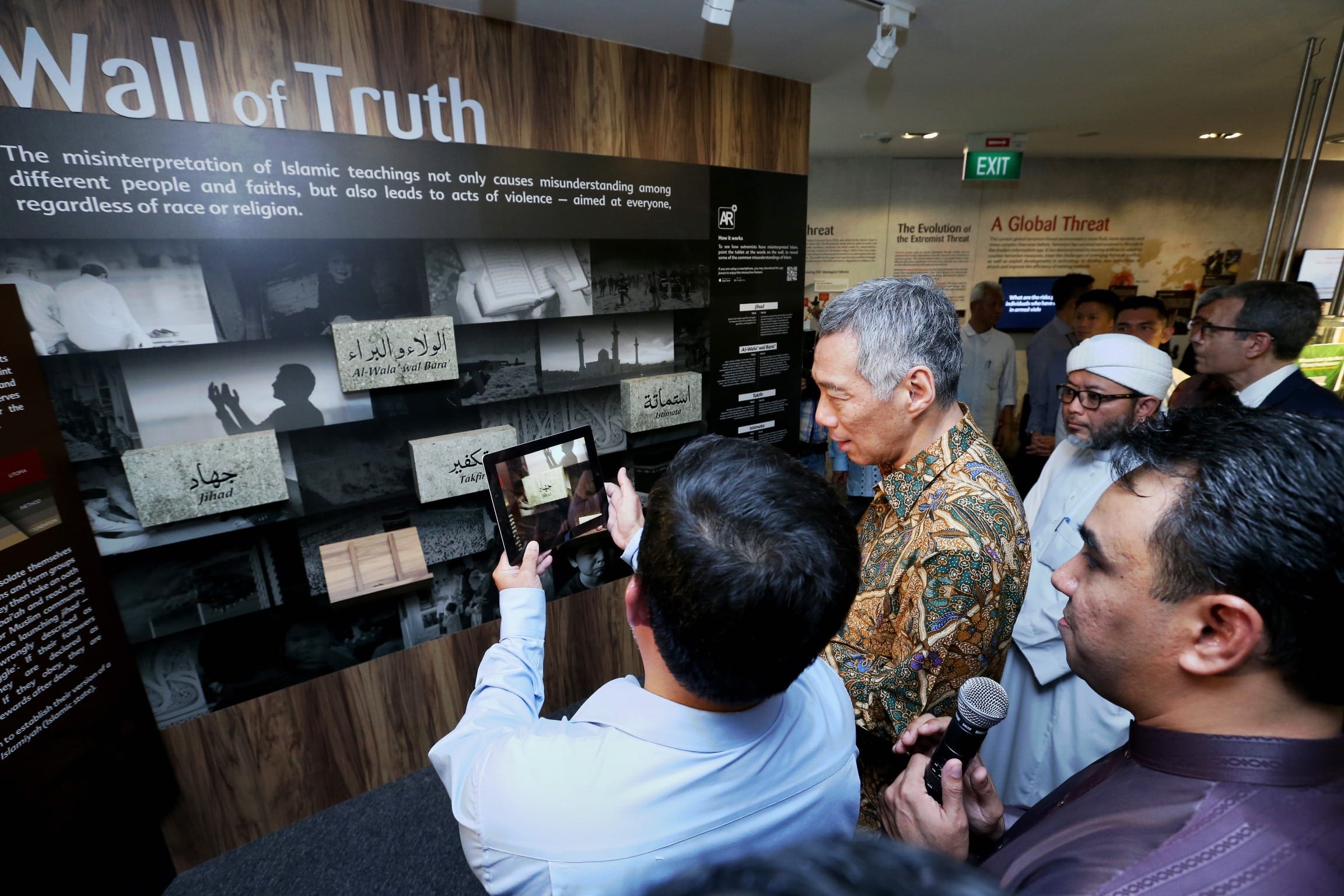 People look at the "Wall of Truth" exhibit, with one using a tablet to view information.