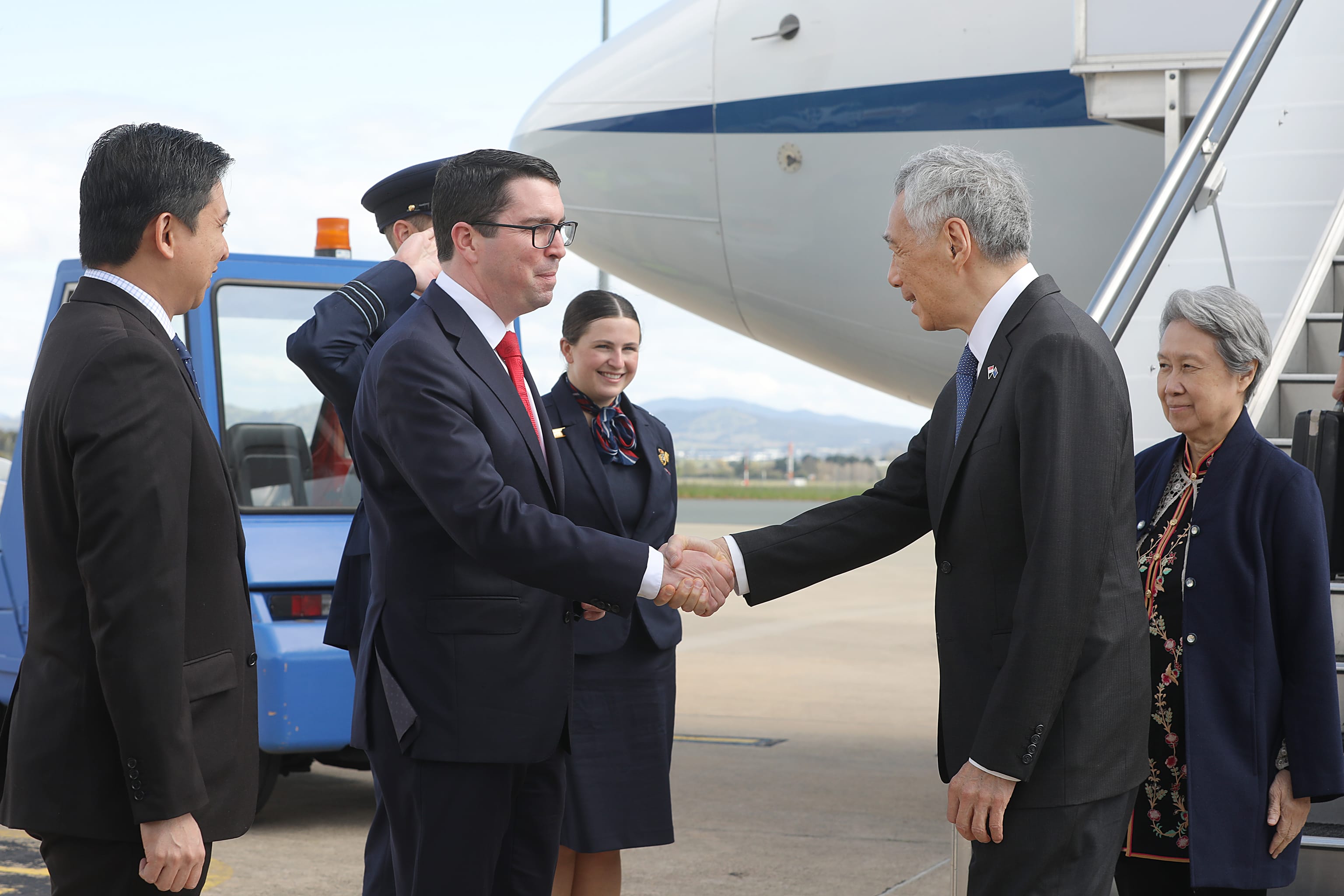 Lee Hsien Loong shakes hands, greeted at aircraft steps; officials surround.
