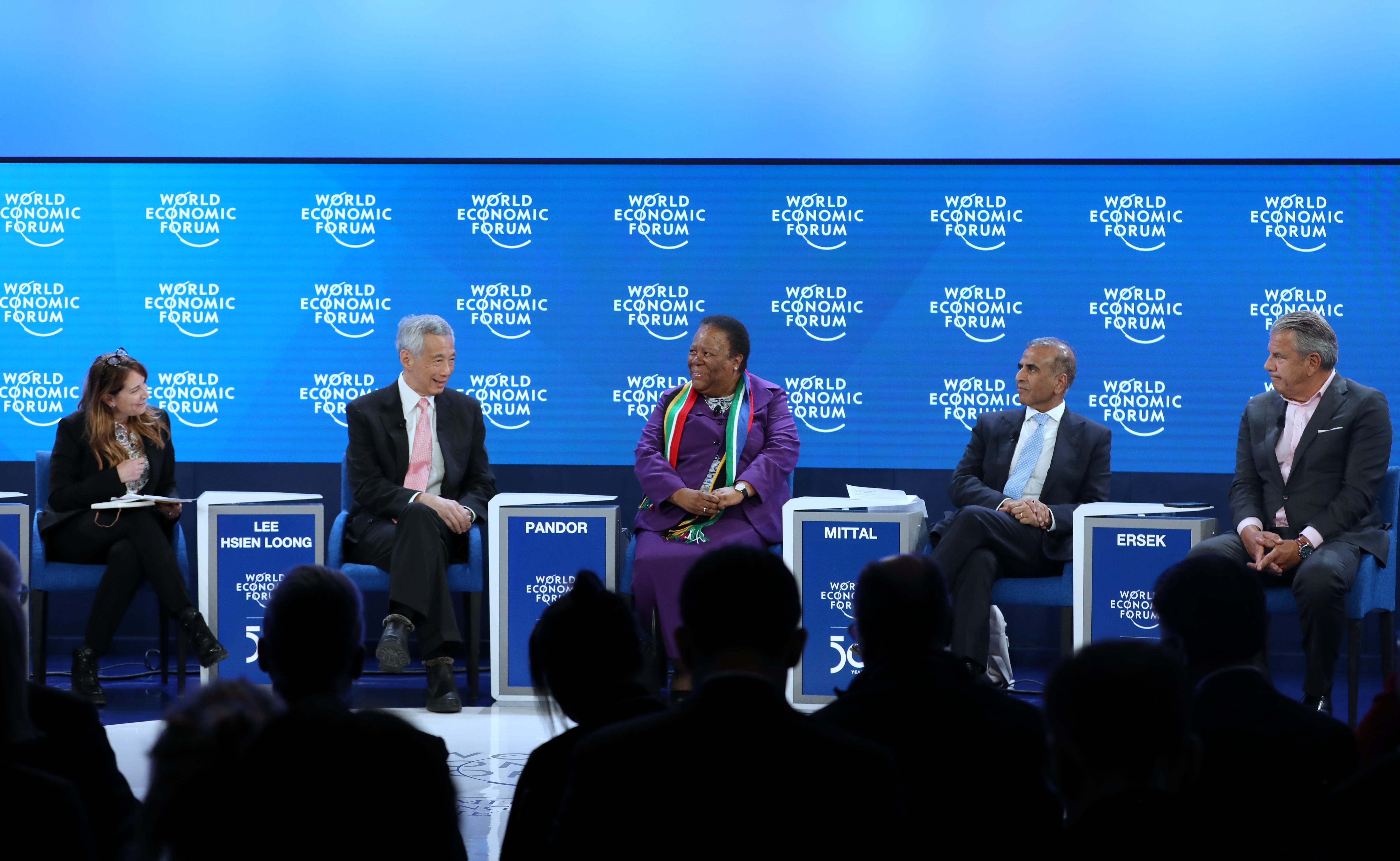 Panel at World Economic Forum with seven people seated on stage, audience in foreground.