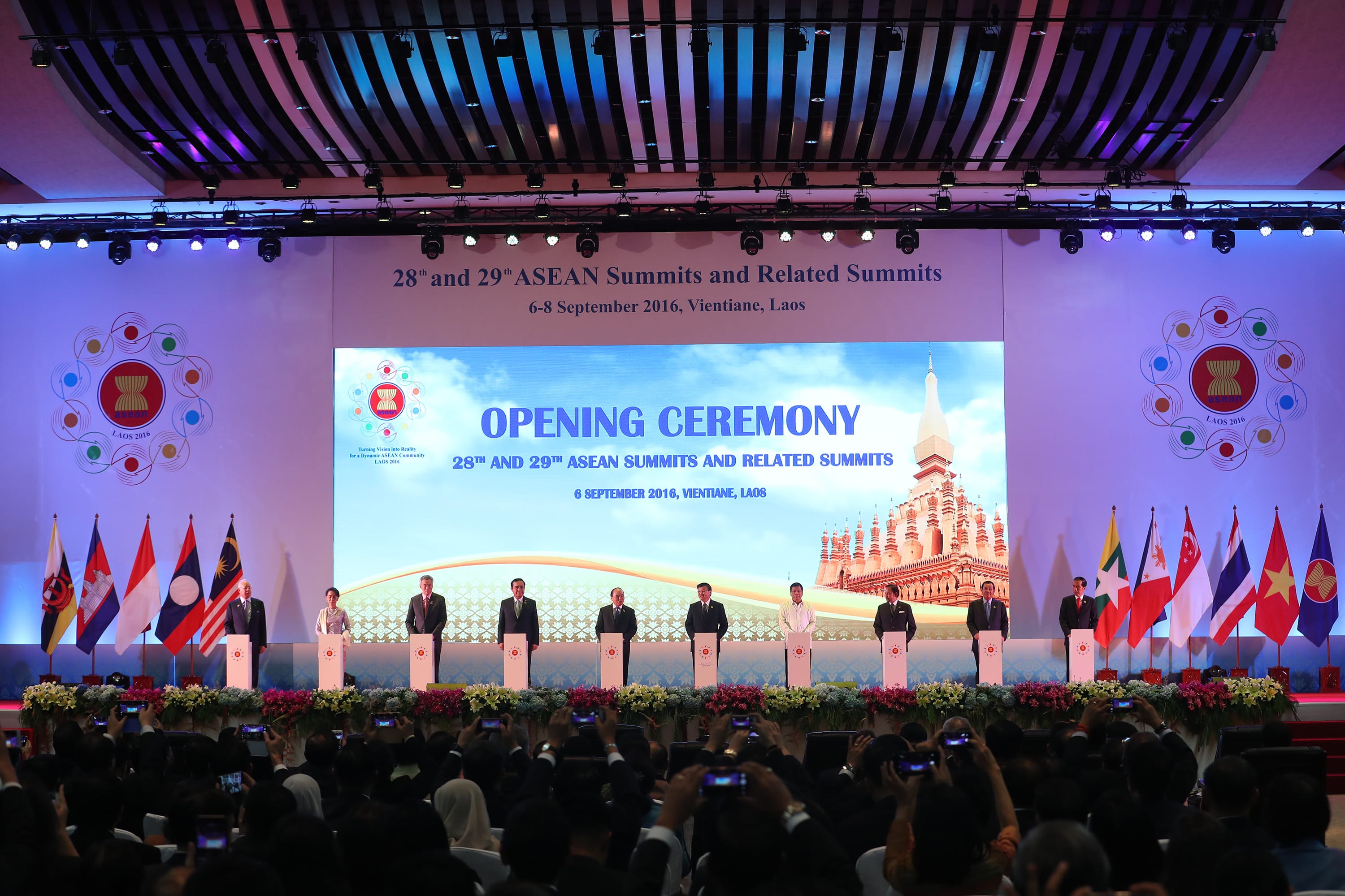 ASEAN summit stage with flags, speakers at podiums, and a large audience.