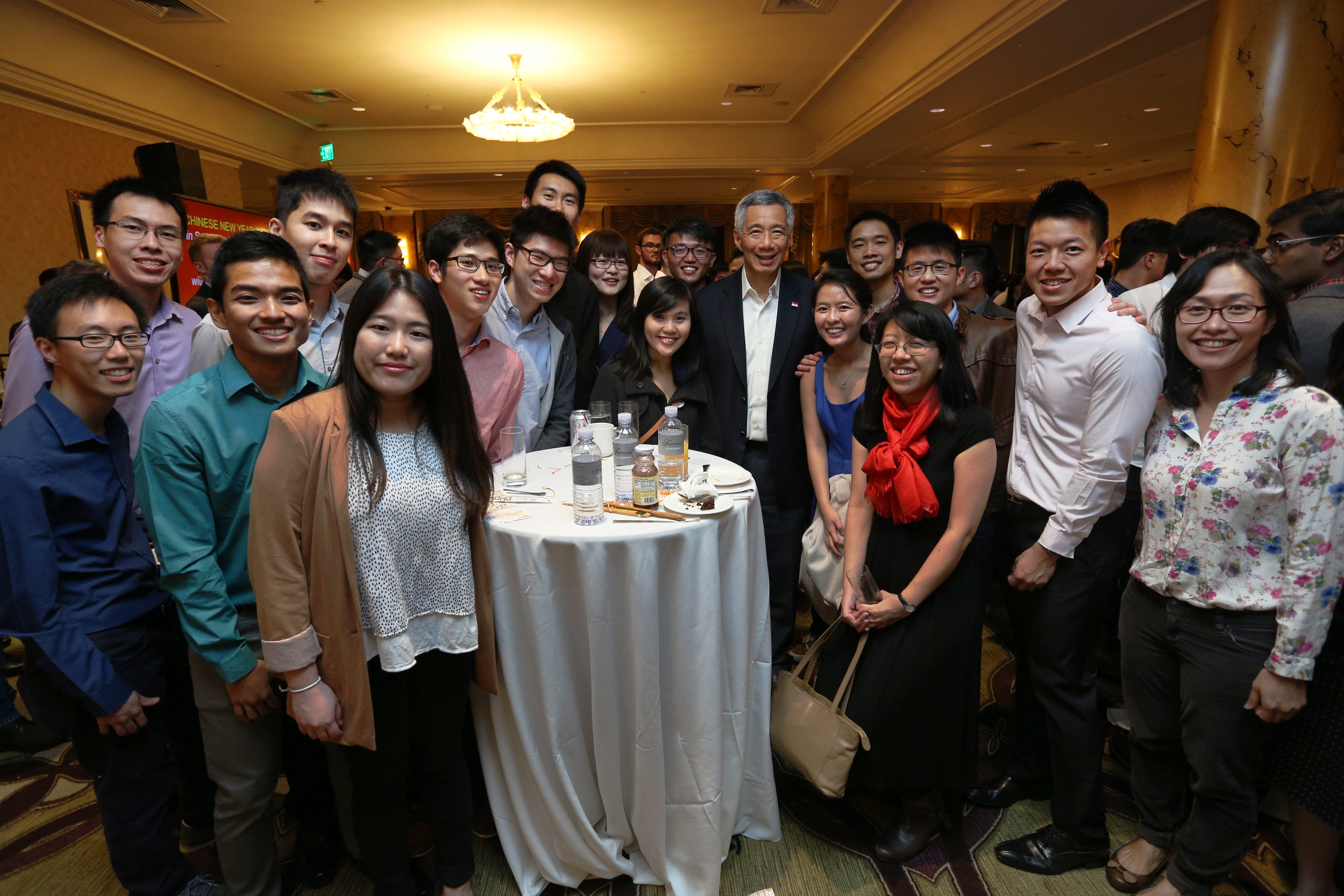 Group poses with Singapore PM Lee Hsien Loong around a white table with drinks in a banquet hall.