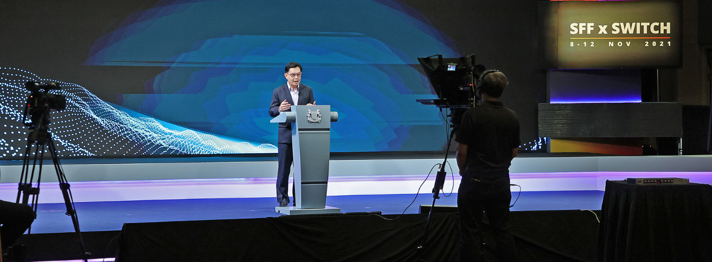 Speaker at podium with SFF x SWITCH backdrop, cameraman in foreground.