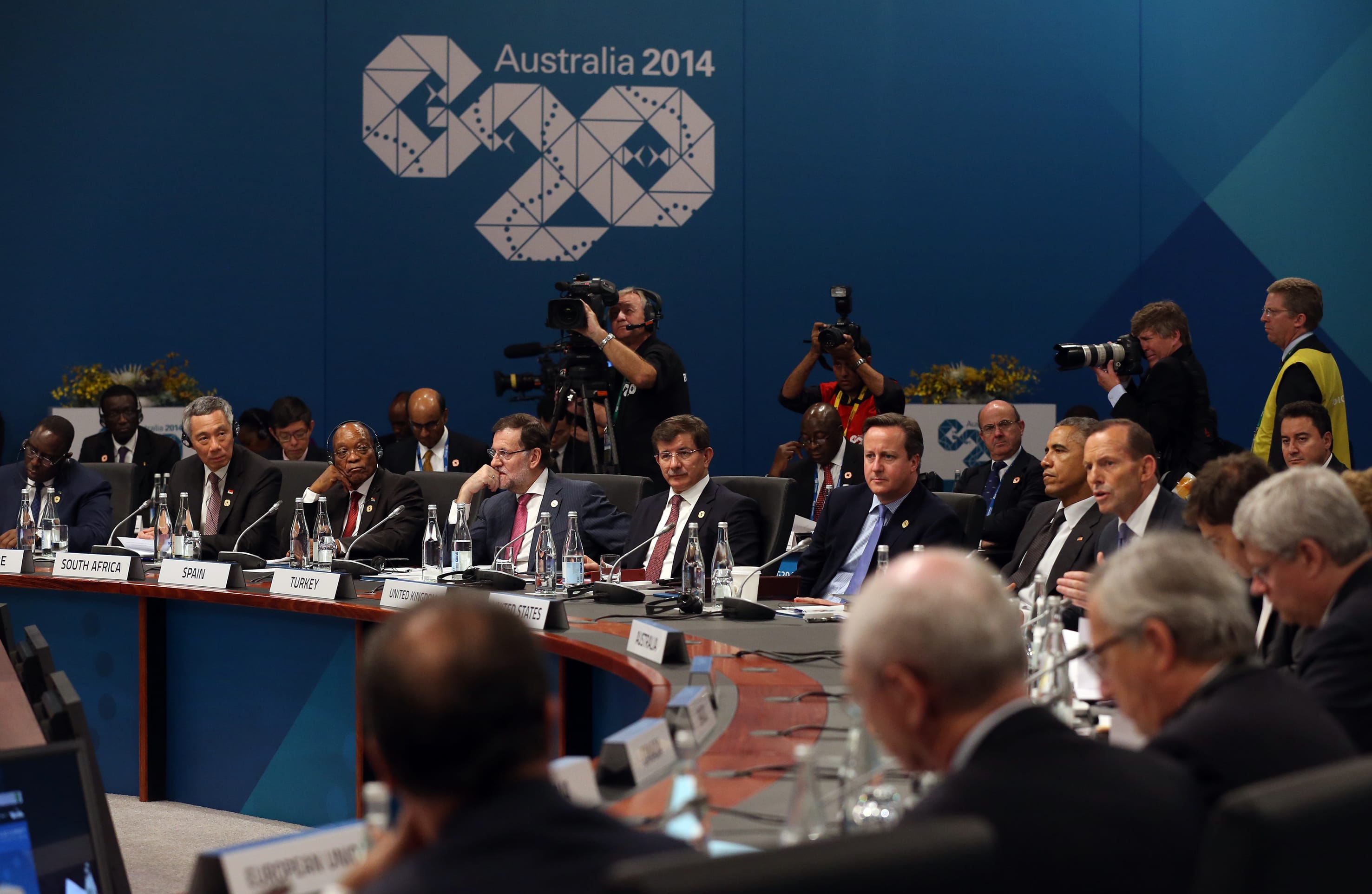 Heads of state at conference table with "Australia 2014" backdrop, photographers in background.
