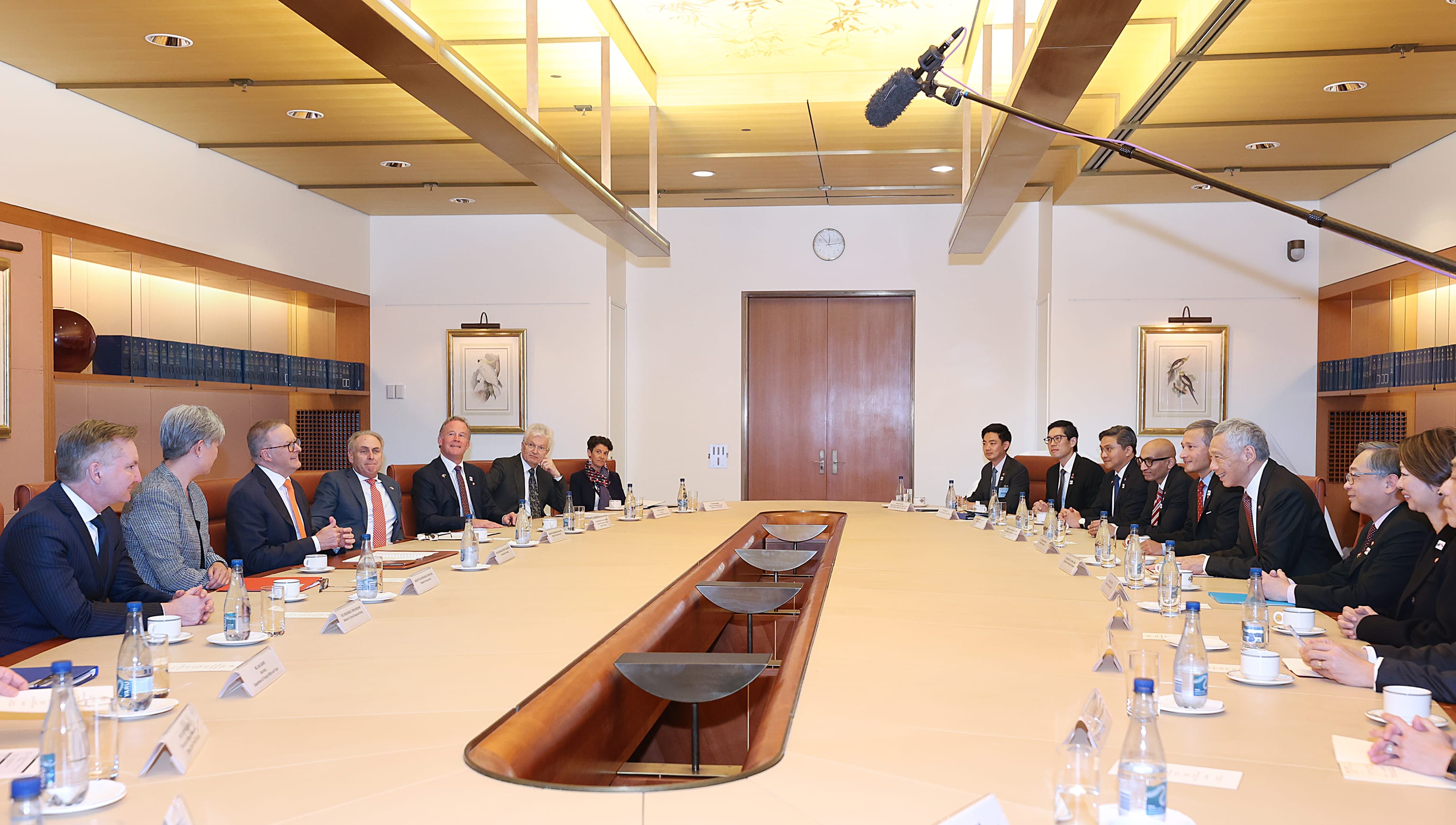People sit at a long table with water bottles and name cards, under a microphone.
