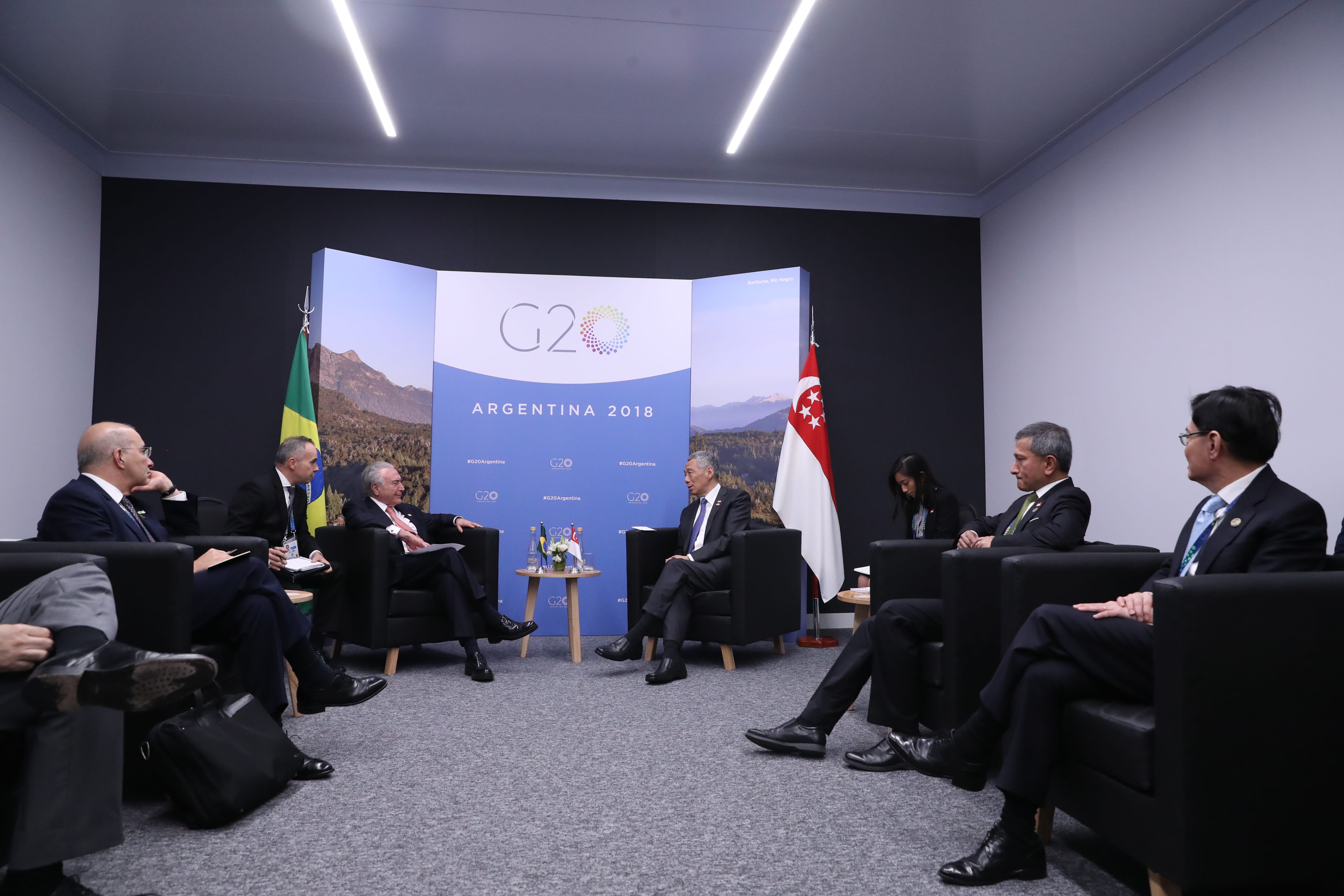 Group of men in suits sitting, G20 Argentina 2018 backdrop, Brazilian and Singaporean flags.
