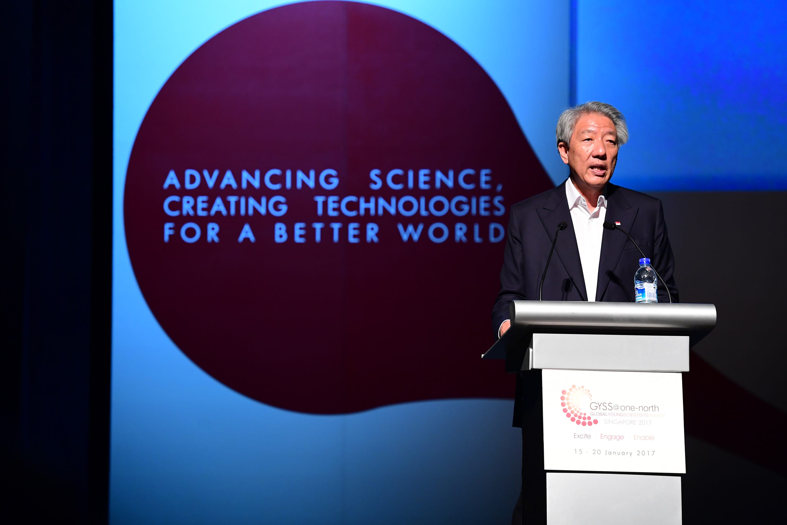 Man in suit at podium with "Advancing Science" graphic for GYSS@one-north 2017.