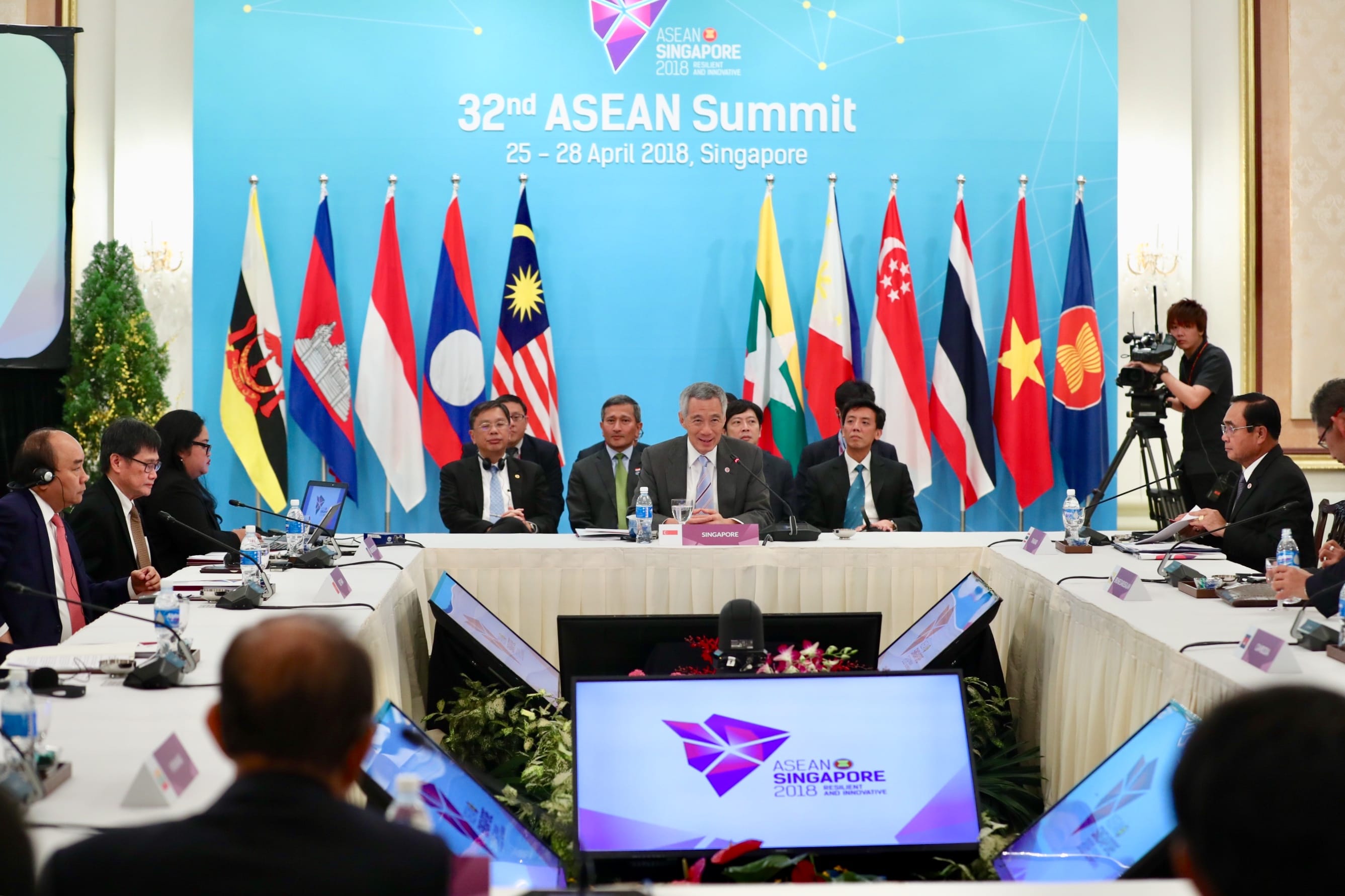 ASEAN Summit meeting with country flags and seated delegates at long tables.