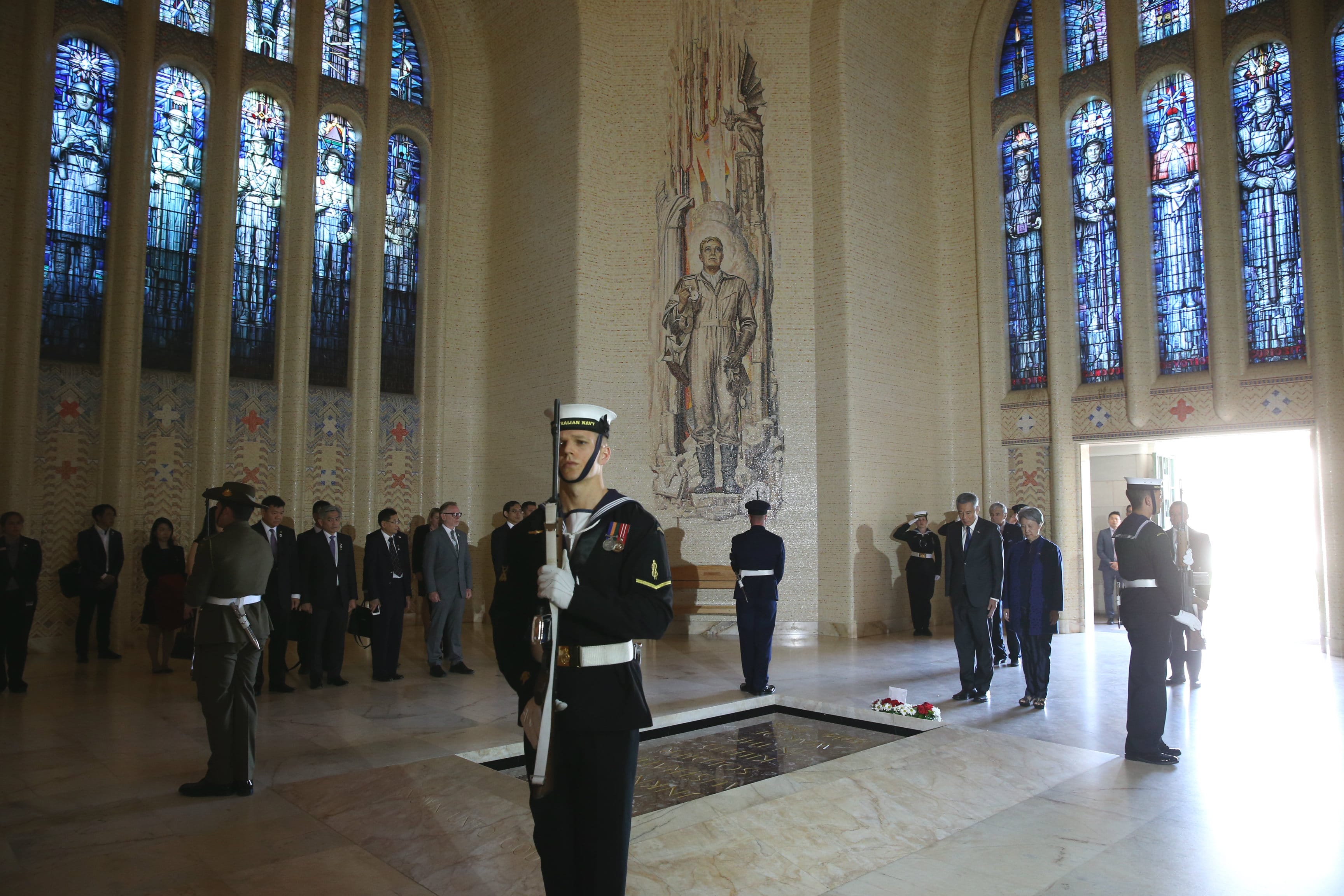Sailor with rifle stands guard in a hall with stained glass, mosaic wall and figures.