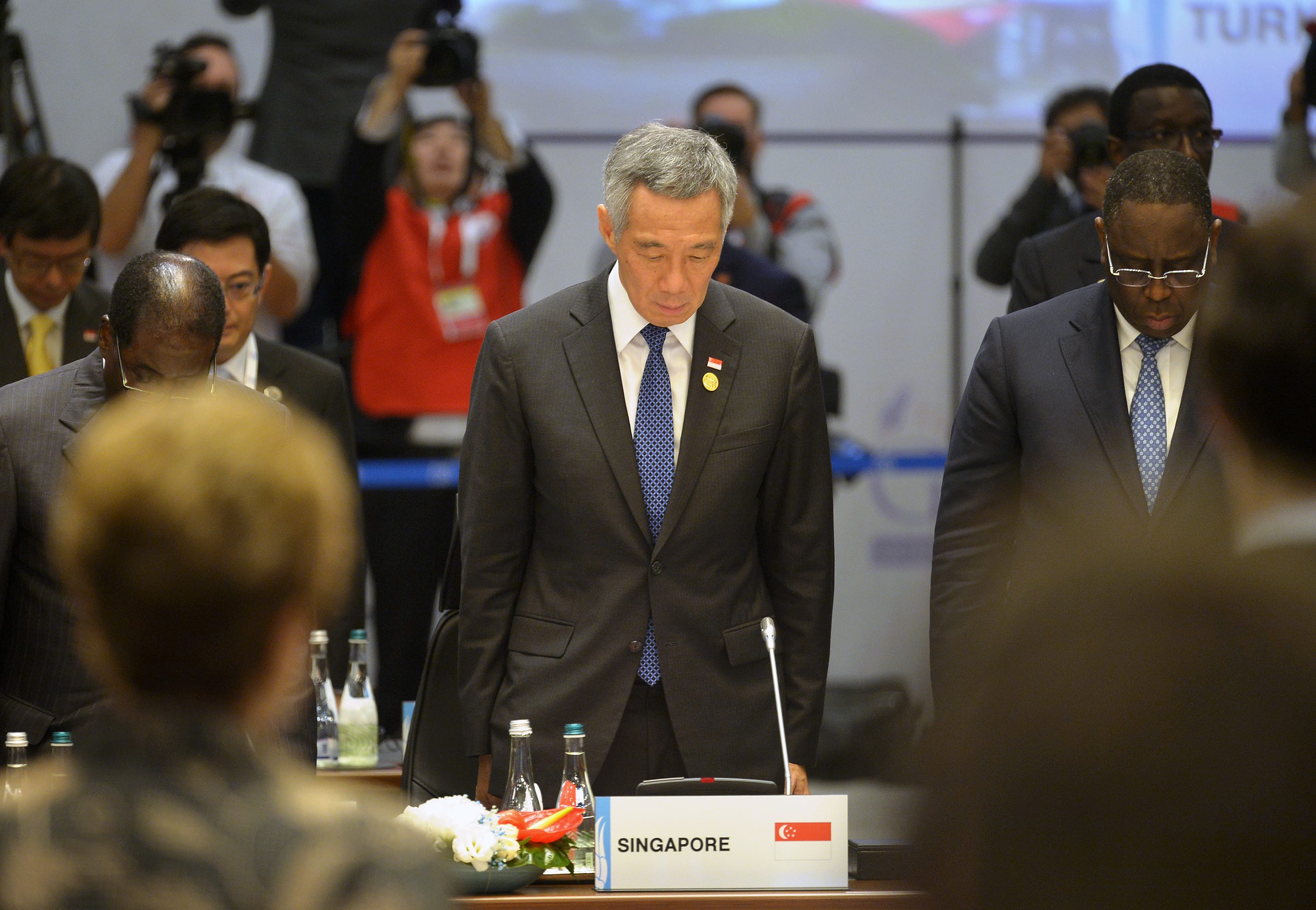 Lee Hsien Loong stands looking down at a table marked "Singapore," surrounded by people.