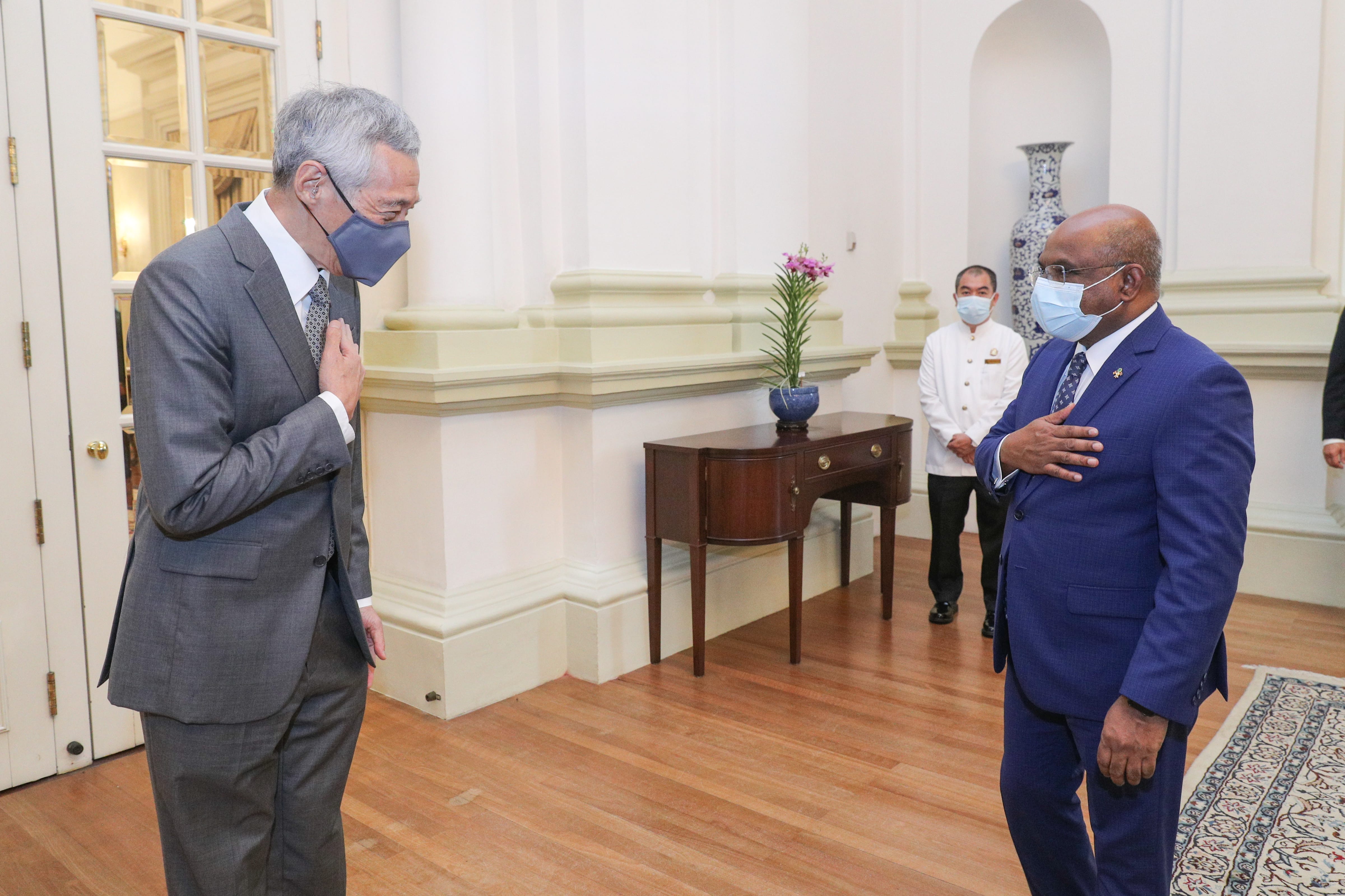 Lee Hsien Loong and Halimah Yacob, both masked, greeting each other indoors.