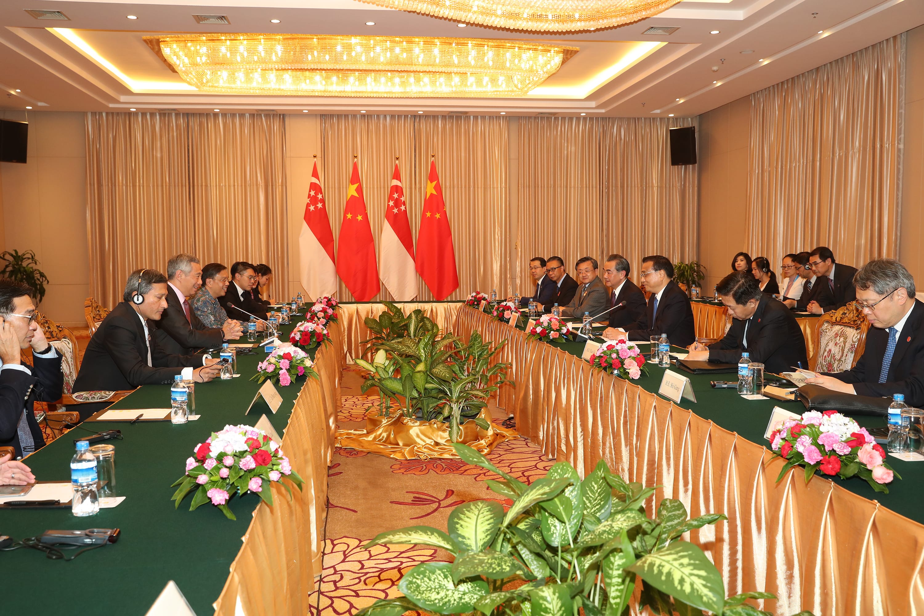 People seated at a long table with Singapore and China flags in the background.