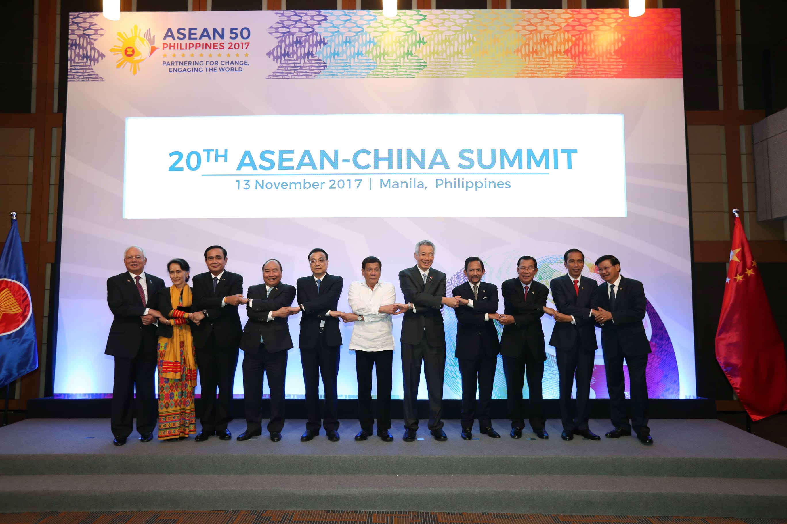 Leaders at 20th ASEAN-China Summit hold hands; flags and branded backdrop visible.