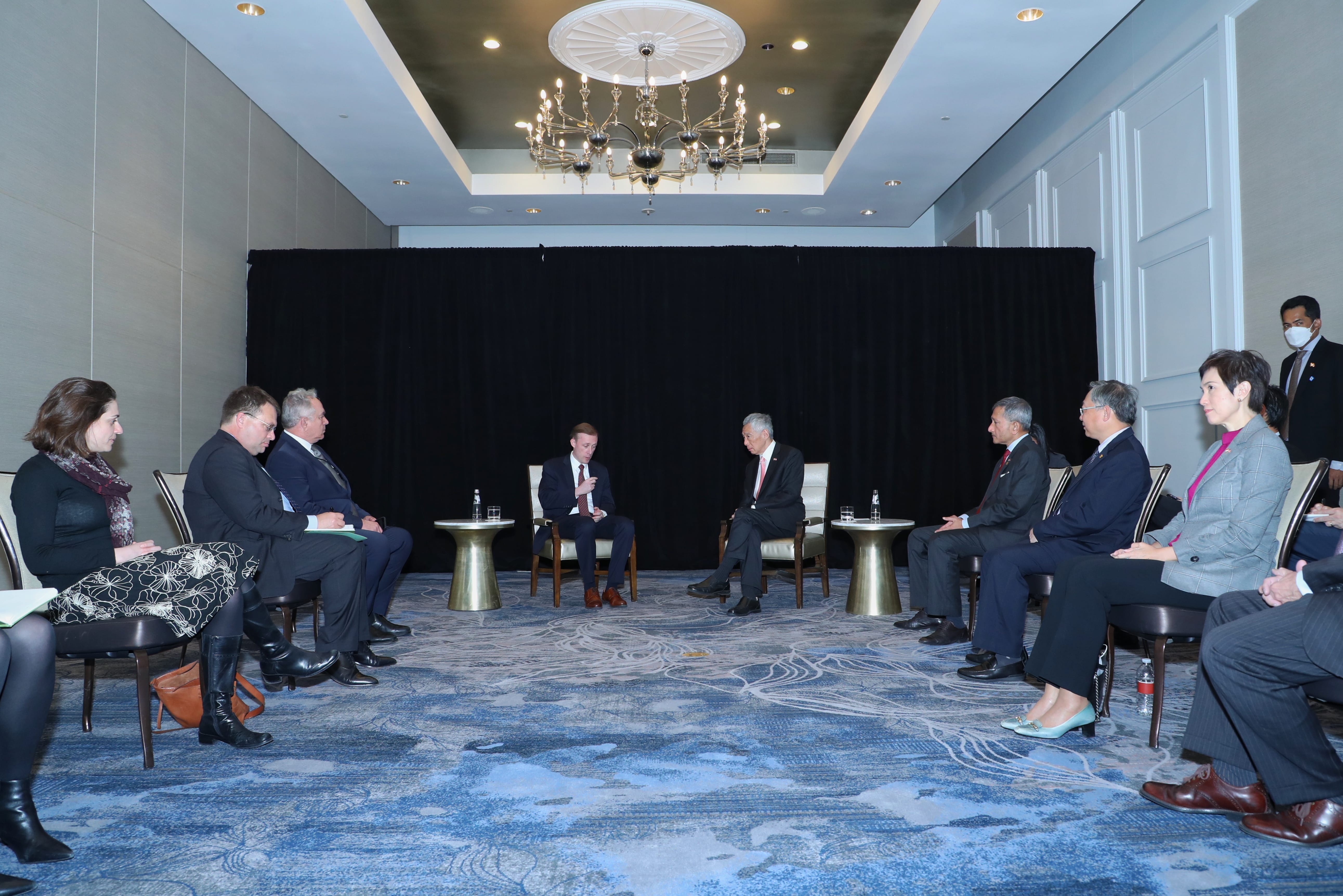 Group of people seated in chairs facing each other in a room with a chandelier.