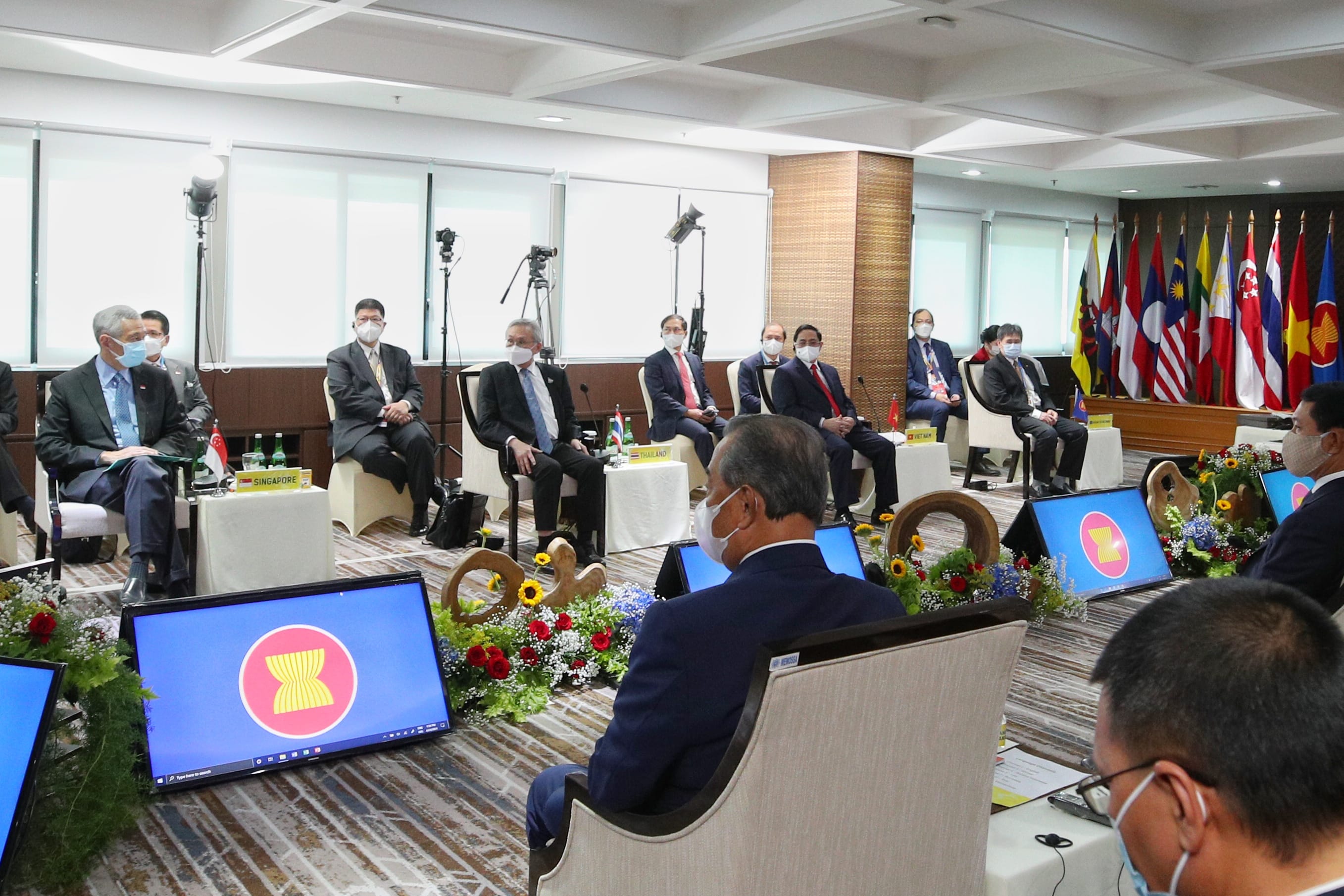 ASEAN summit with officials masked, seated before country flags and logo screens.