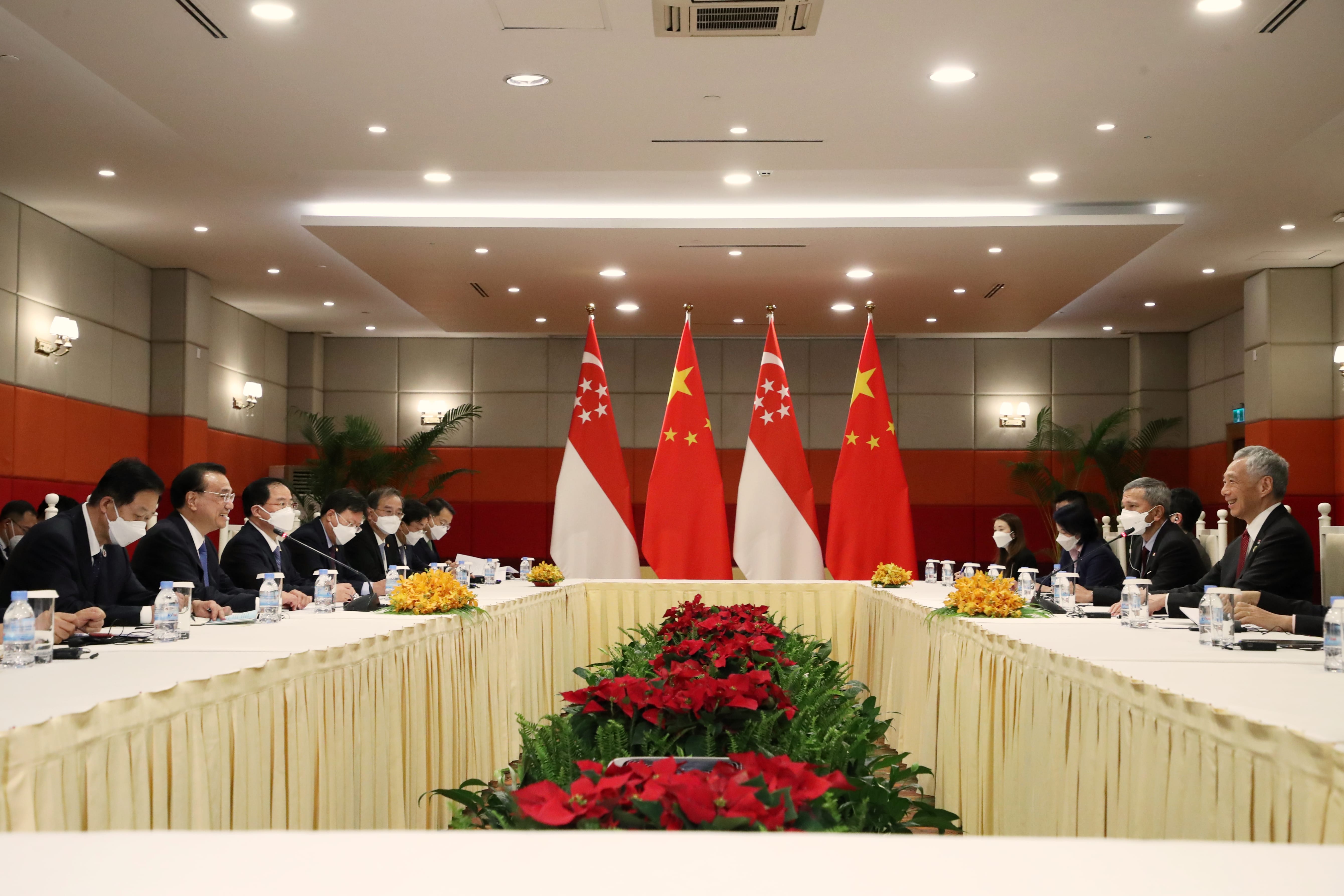 Meeting room with flags of Singapore and China, long table with seated attendees wearing face masks.