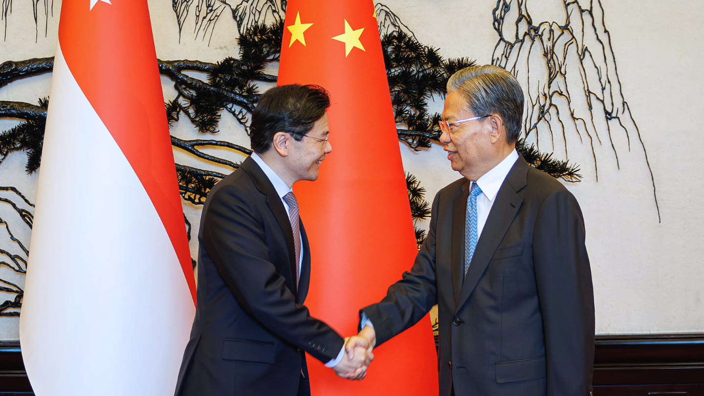 Two men in suits shaking hands near Singapore and China flags.